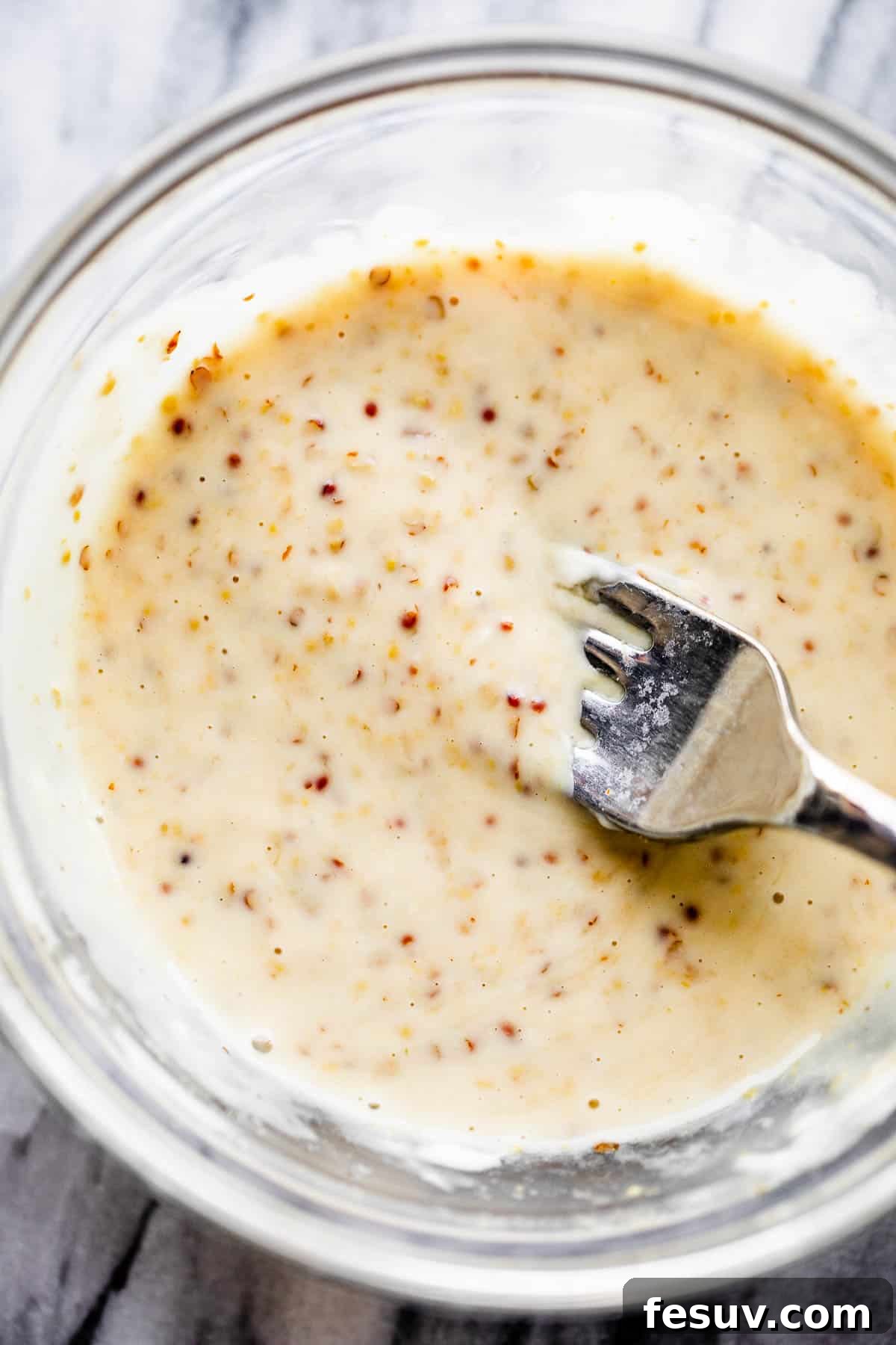 This baked Maple Mustard Salmon recipe is lightly seasoned, then brushed with a sweet and tangy sauce made from maple syrup and Dijon mustard! A glass bowl with stone-ground Dijon mustard, mayonnaise, and maple syrup being whisked together to form the salmon glaze.