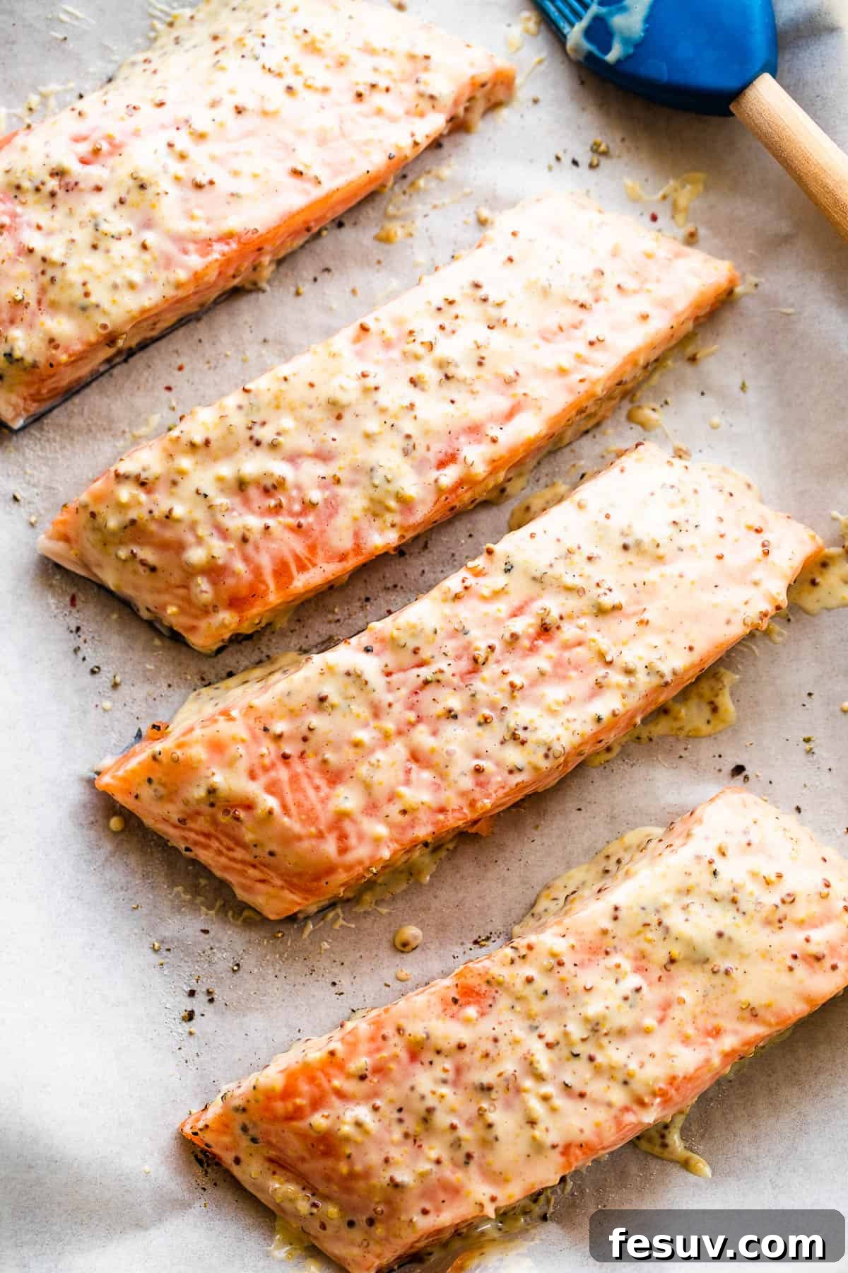 This baked Maple Mustard Salmon recipe is lightly seasoned, then brushed with a sweet and tangy sauce made from maple syrup and Dijon mustard! Four raw salmon fillets arranged neatly on a parchment-lined baking sheet, ready for seasoning and glazing.