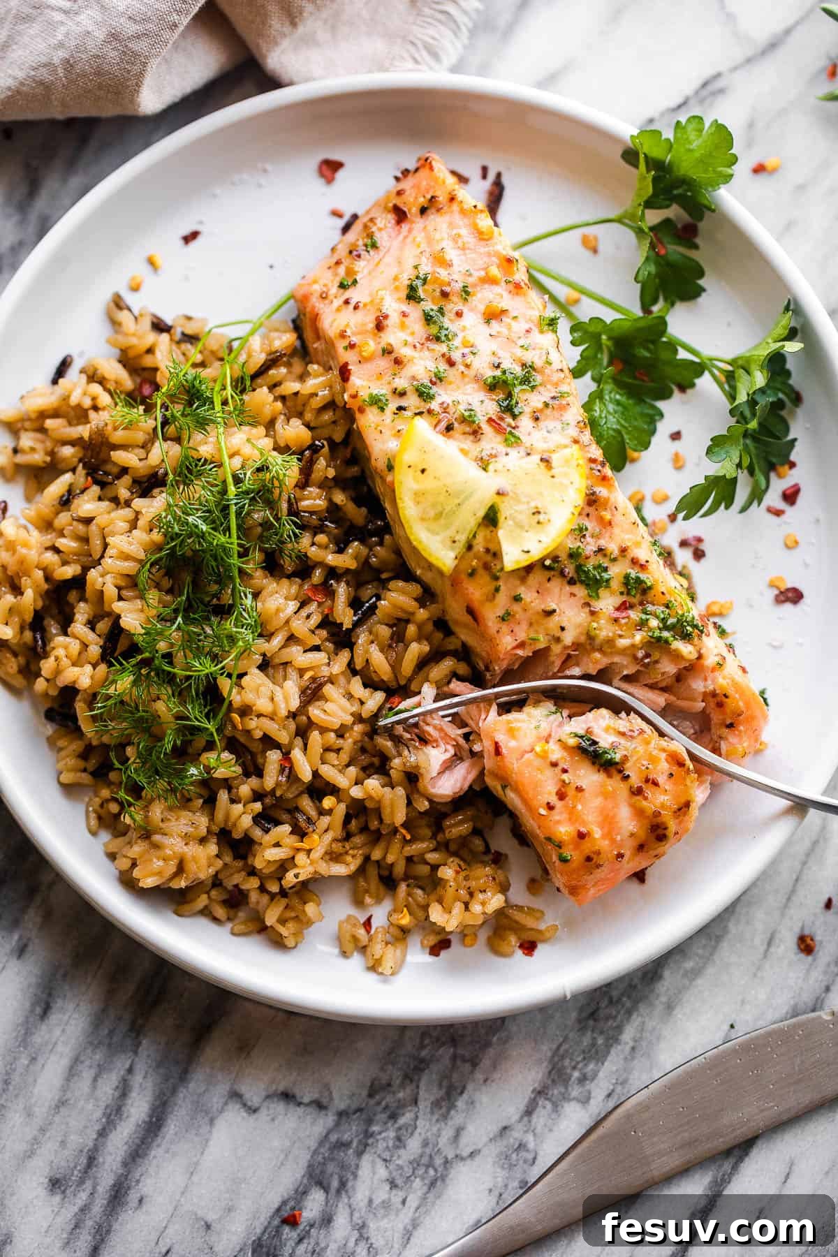 This baked Maple Mustard Salmon recipe is lightly seasoned, then brushed with a sweet and tangy sauce made from maple syrup and Dijon mustard! A baked maple mustard salmon fillet served on a white plate with a side of wild brown rice and fresh herbs.