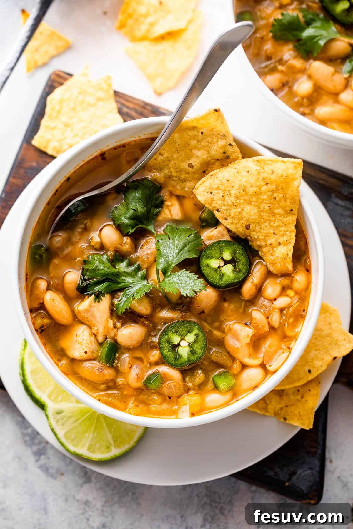 Overhead shot of two white soup bowls filled with delicious chicken chili, garnished with fresh cilantro and a dollop of sour cream.