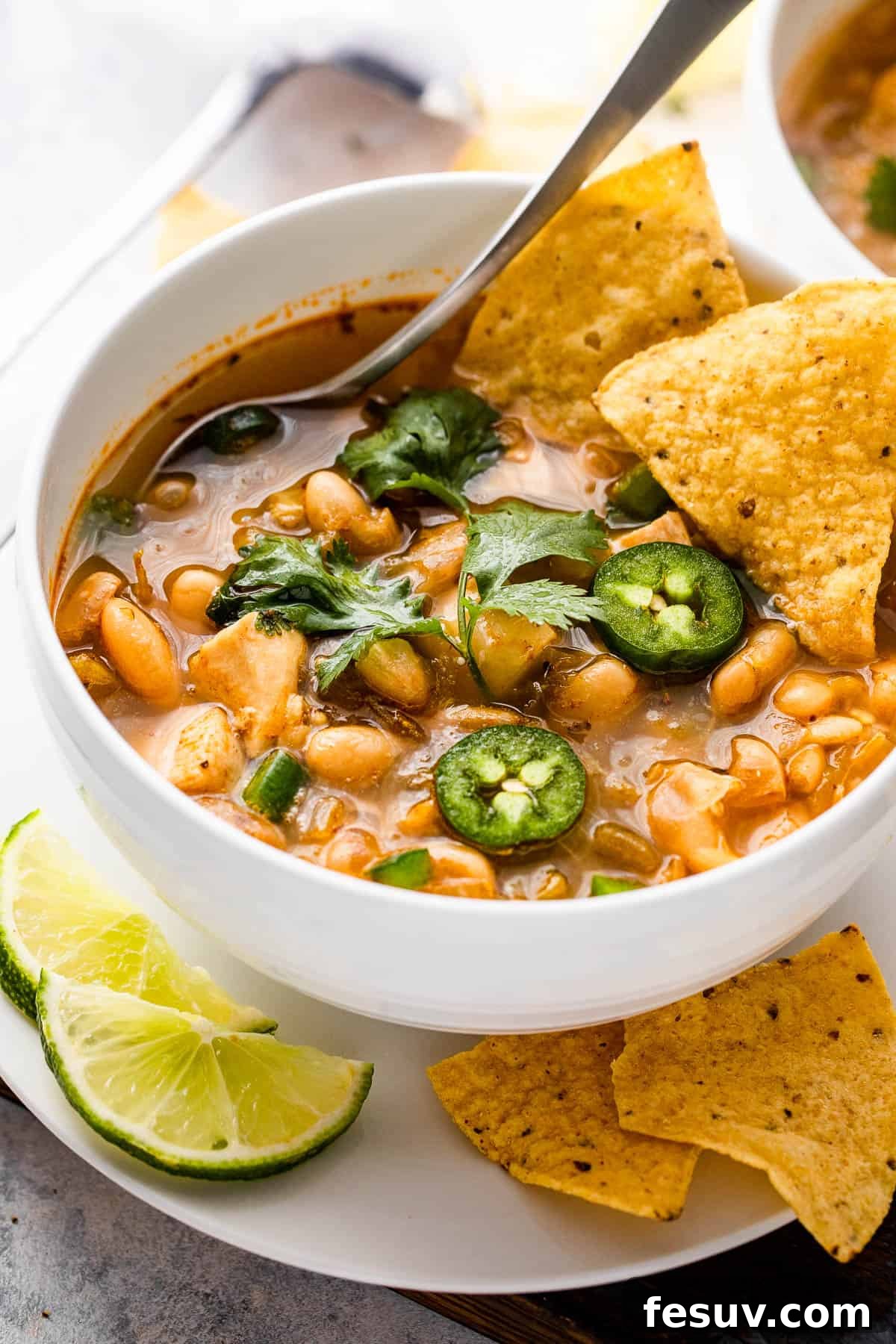 Close-up side view of a steaming bowl of chicken chili, generously topped with sliced jalapeños and crispy tortilla chips, ready to be enjoyed.