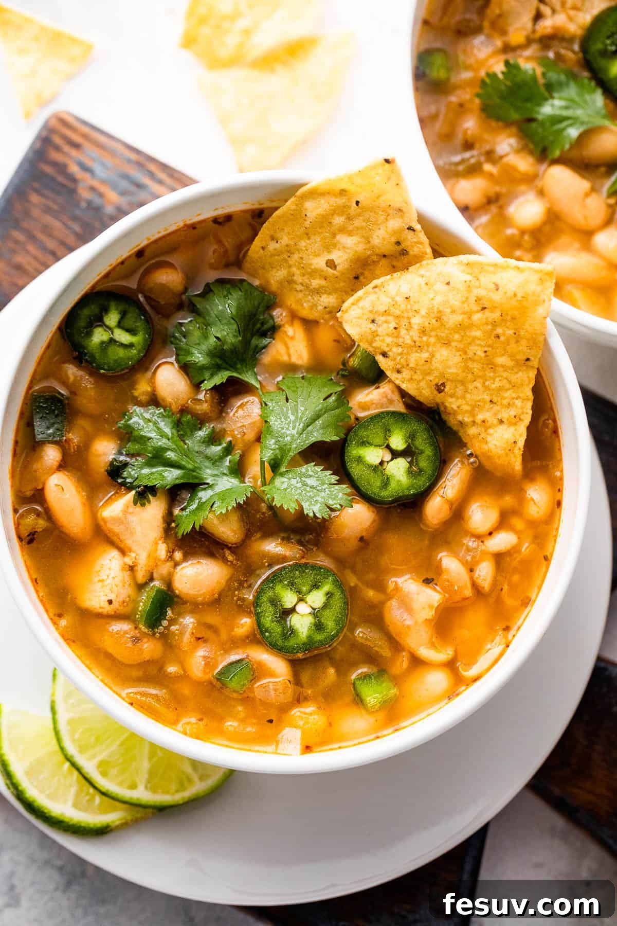 Overhead shot of two white soup bowls, each holding a generous serving of chicken chili, garnished simply and ready to be enjoyed.