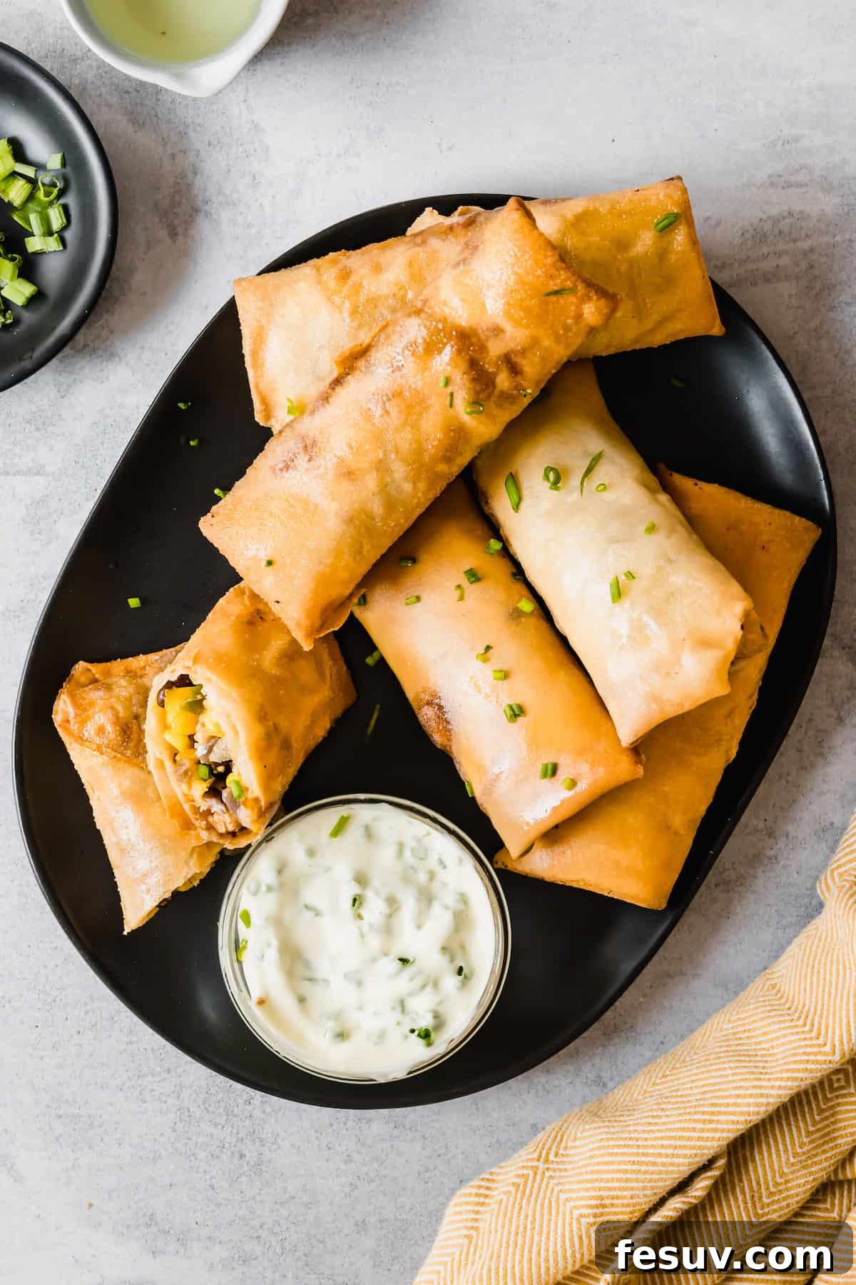 Homemade Egg Rolls on a Black Plate with a Container of Dipping Sauce