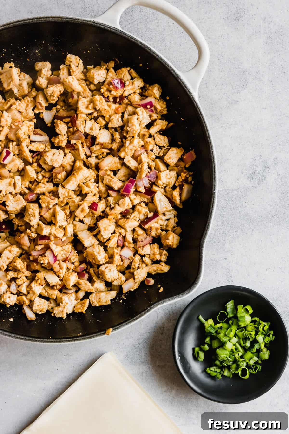 Spices, Diced Chicken and Onions in a Pan Next to a Dish of Chopped Scallions