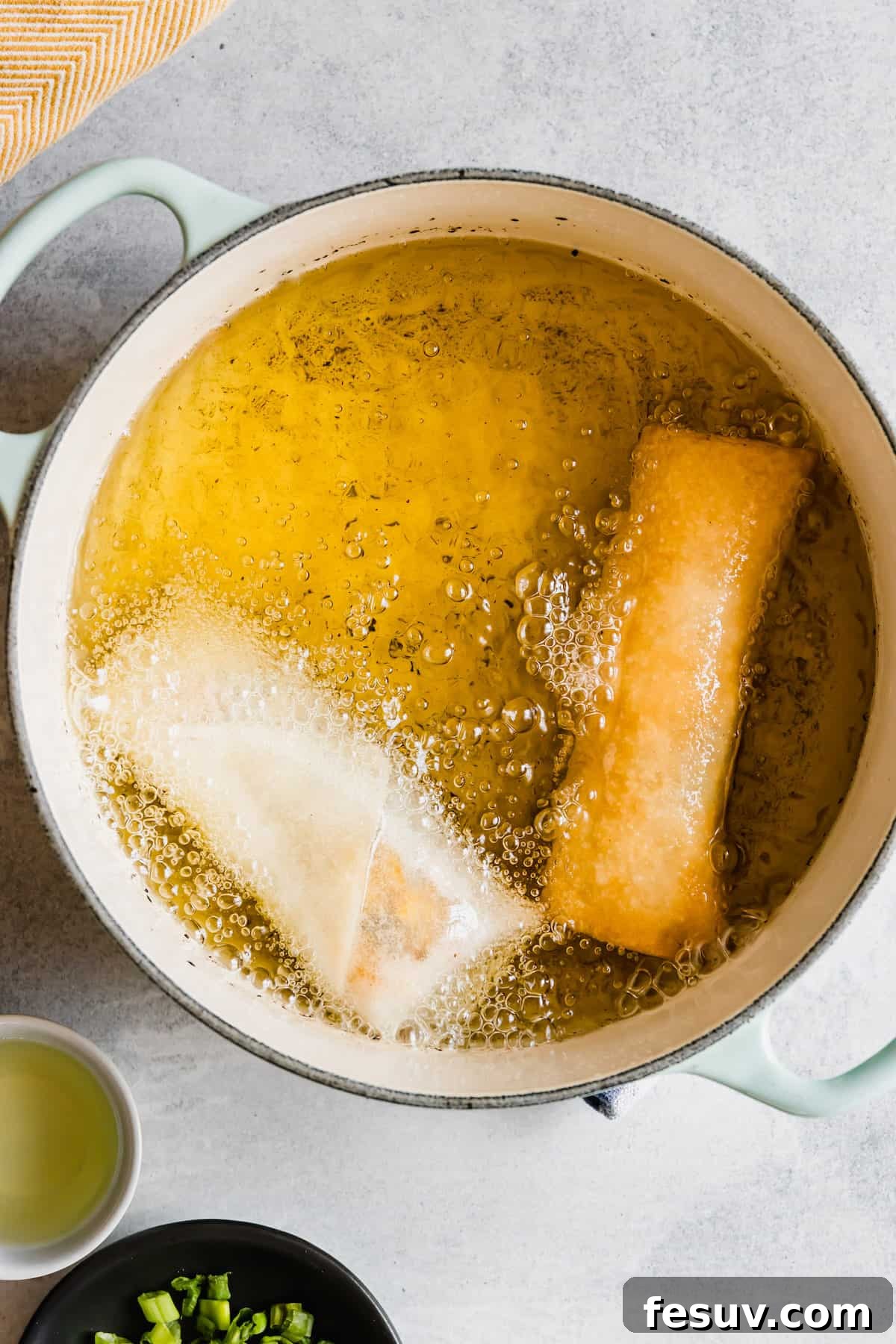 Two Egg Rolls Frying in a Double-Handle Pan with Oil