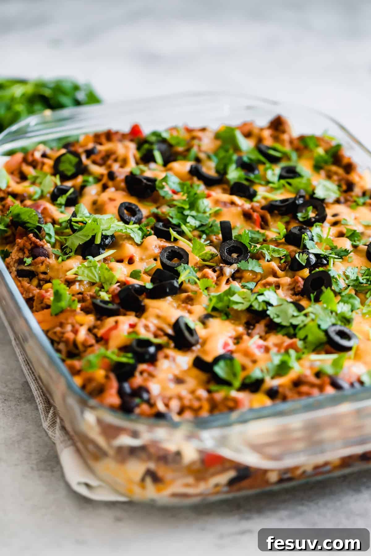 Enchilada Lasagna 13 A hearty Taco Casserole in a clear glass baking pan, resting on a white and tan dish towel, ready for serving.