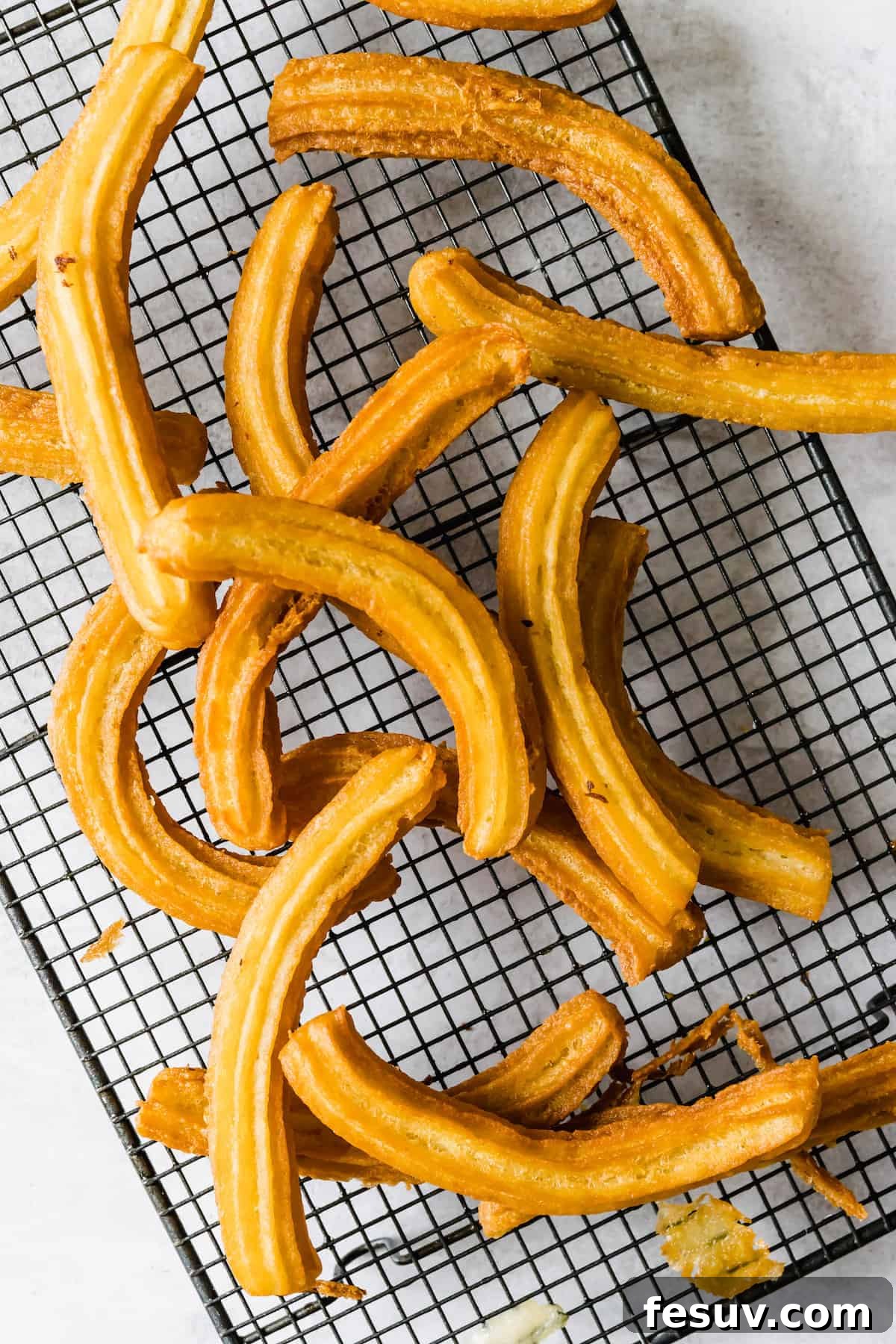 Perfect Homemade Churros 7 Sixteen freshly fried churros neatly arranged on a wire cooling rack.