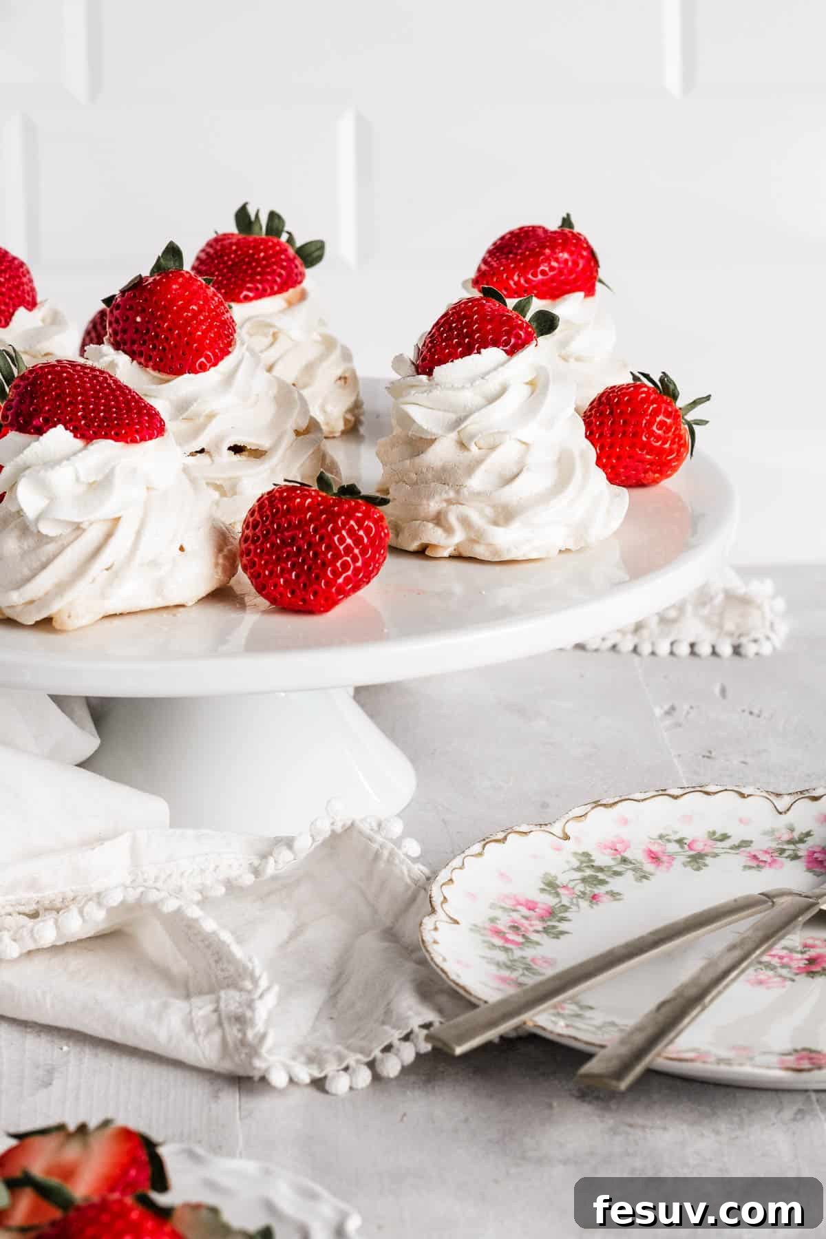 Mini pavlovas on a cake plate topped with whipped cream and strawberries
