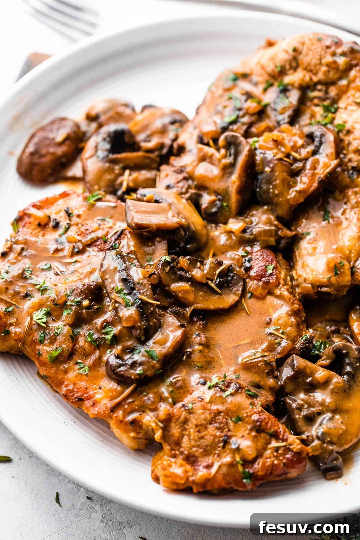 Perfectly Tender Instant Pot Pork Chops 3 Two generously sauced bone-in pork chops presented on a pristine white plate, adorned with creamy mushroom gravy and a sprinkle of fresh herbs.