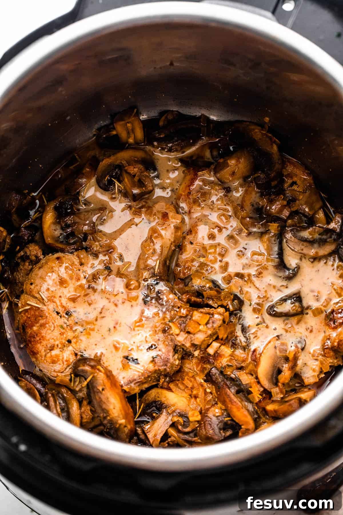 Perfectly Tender Instant Pot Pork Chops 5 Overhead perspective of two succulent pork chops nestled in the Instant Pot, beautifully covered in a rich and glossy creamy mushroom gravy sauce.