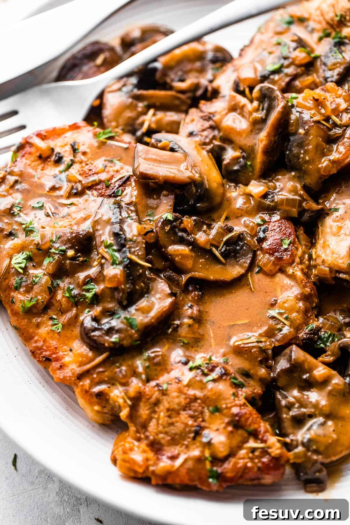 Perfectly Tender Instant Pot Pork Chops 6 Two perfectly cooked bone-in pork chops resting on a white serving plate, luxuriating under a generous coating of creamy mushroom gravy.