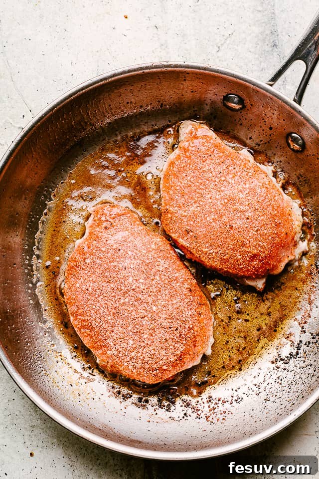 Juicy, tender, and flavorful, these garlic parmesan pan fried pork chops are smothered in a rich honey garlic sauce. Done in just 20 minutes! Seasoned pork chops searing in a hot skillet with butter and olive oil.