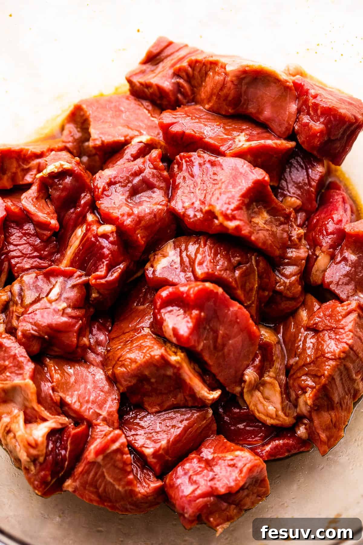 Raw sirloin steak bites marinating in a glass bowl with a dark, savory sauce