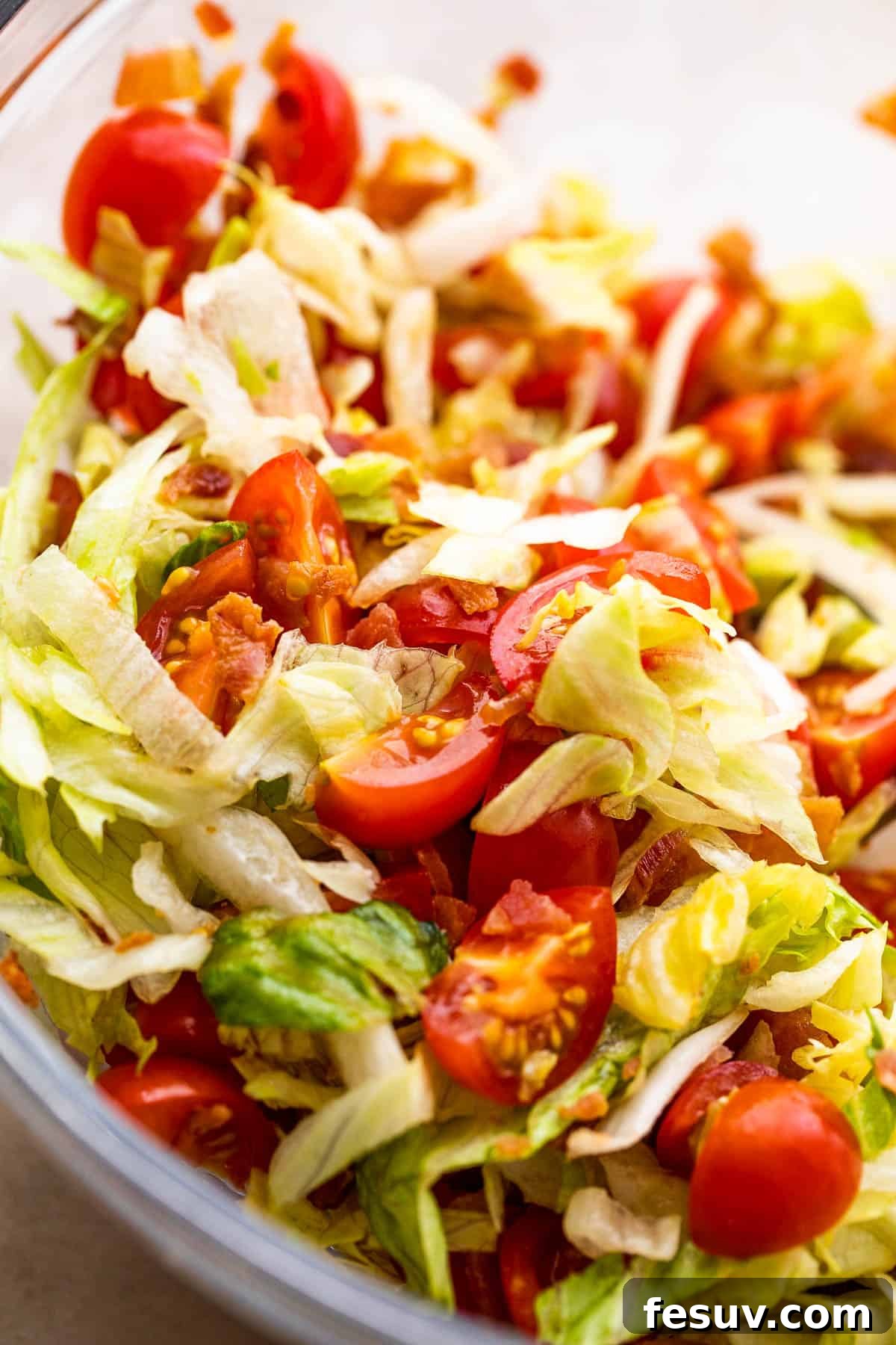 A vibrant mix of bacon, lettuce, and quartered cherry tomatoes tossed in balsamic dressing in a clear glass bowl, ready to be spooned onto bruschetta