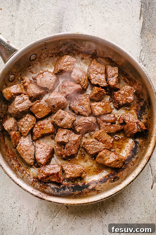 Searing cubed beef tips in a hot skillet to develop a golden-brown crust.