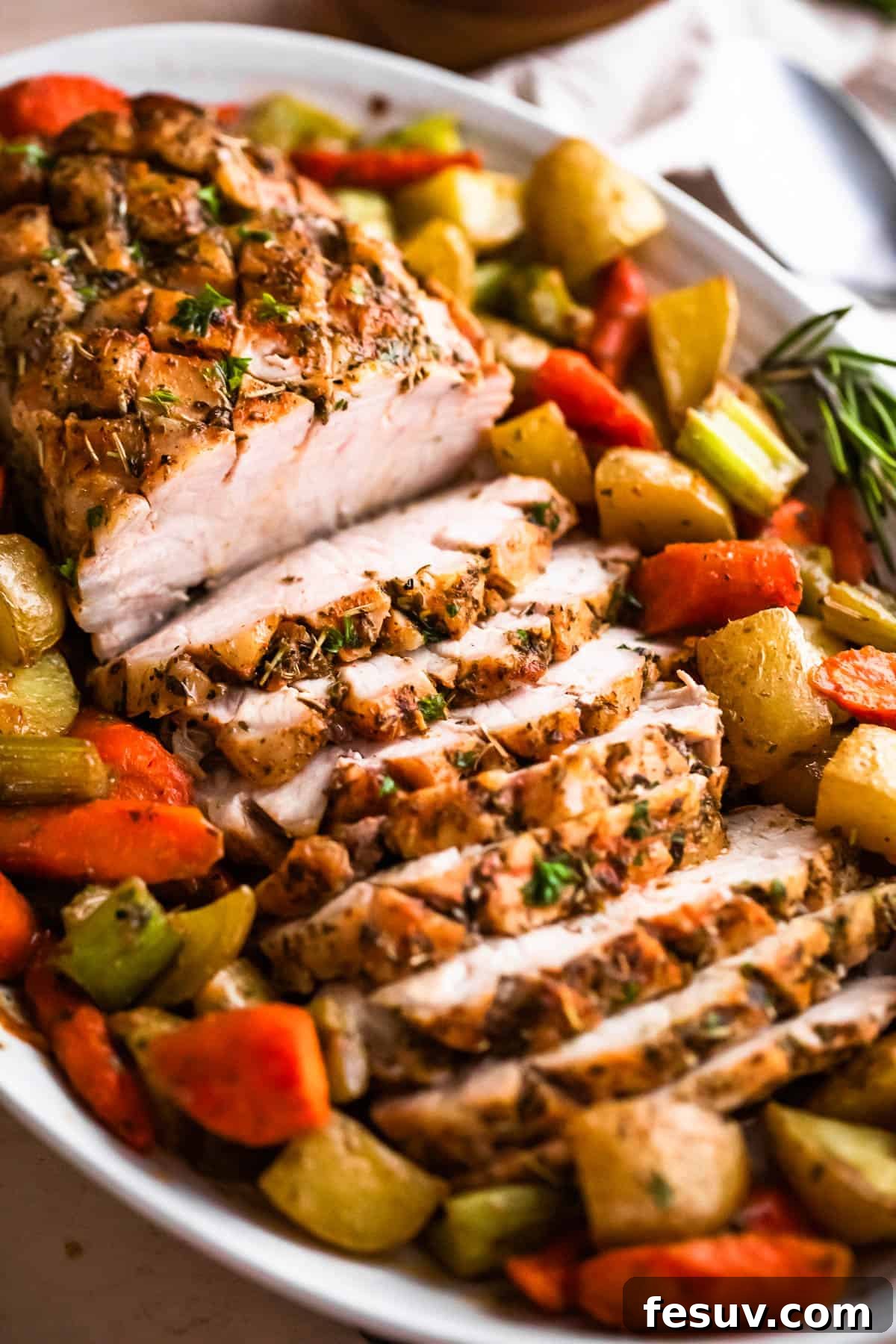Herb-Crusted Pork Loin with Roasted Root Vegetables 2 side shot of oval plate with cooked and sliced pork loin roast and roasted vegetables arranged around the roast
