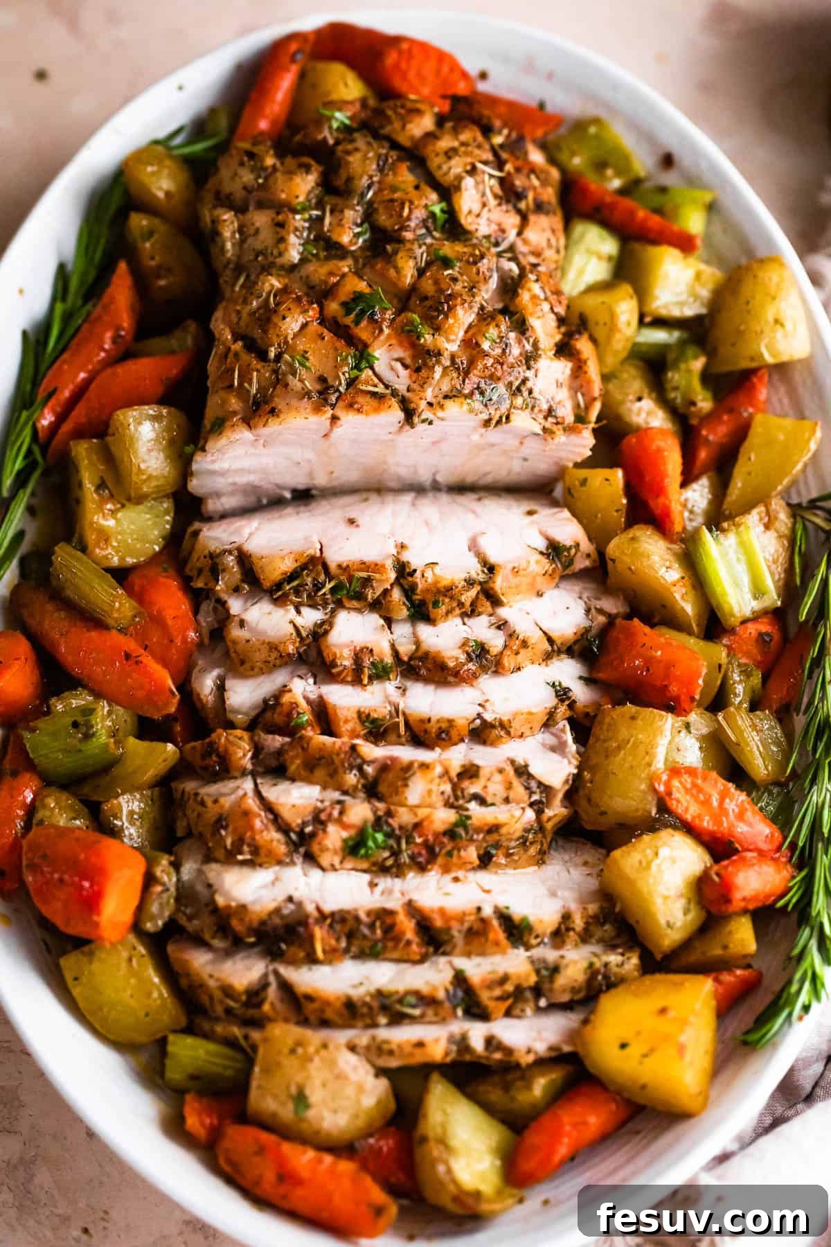 Herb-Crusted Pork Loin with Roasted Root Vegetables 3 overhead shot of oval plate with cooked and sliced pork loin roast and roasted vegetables arranged around the roast