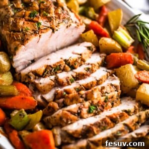 Herb-Crusted Pork Loin with Roasted Root Vegetables 9 side shot of oval plate with cooked and sliced pork loin roast and roasted vegetables arranged around the roast
