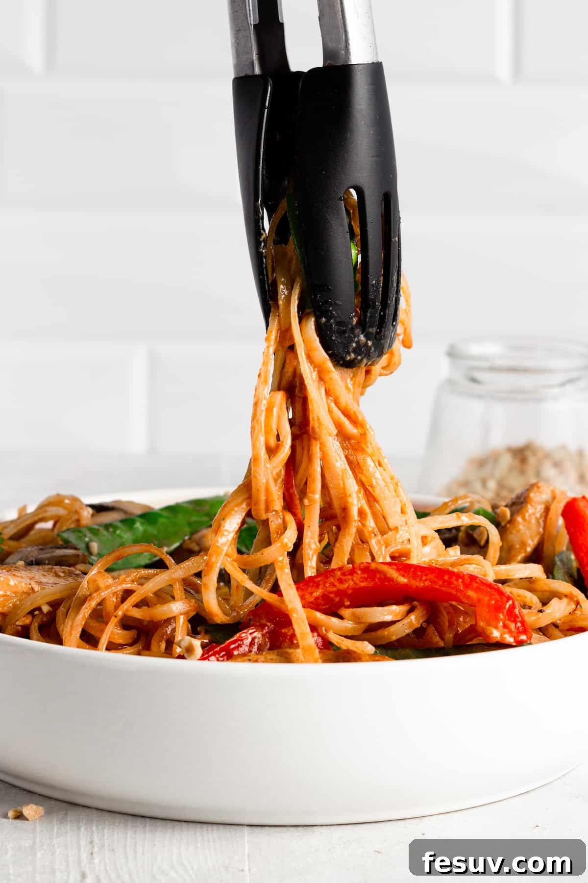 Flavorful Chicken Noodle Stir-Fry 4 Tongs Scooping Up Some Noodles Out of a Bowl of Chicken Lo Mein