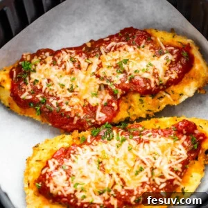 Two Pieces of Breaded, Partially Cooked Chicken Being Topped with Marinara and Shredded Parmesan Cheese