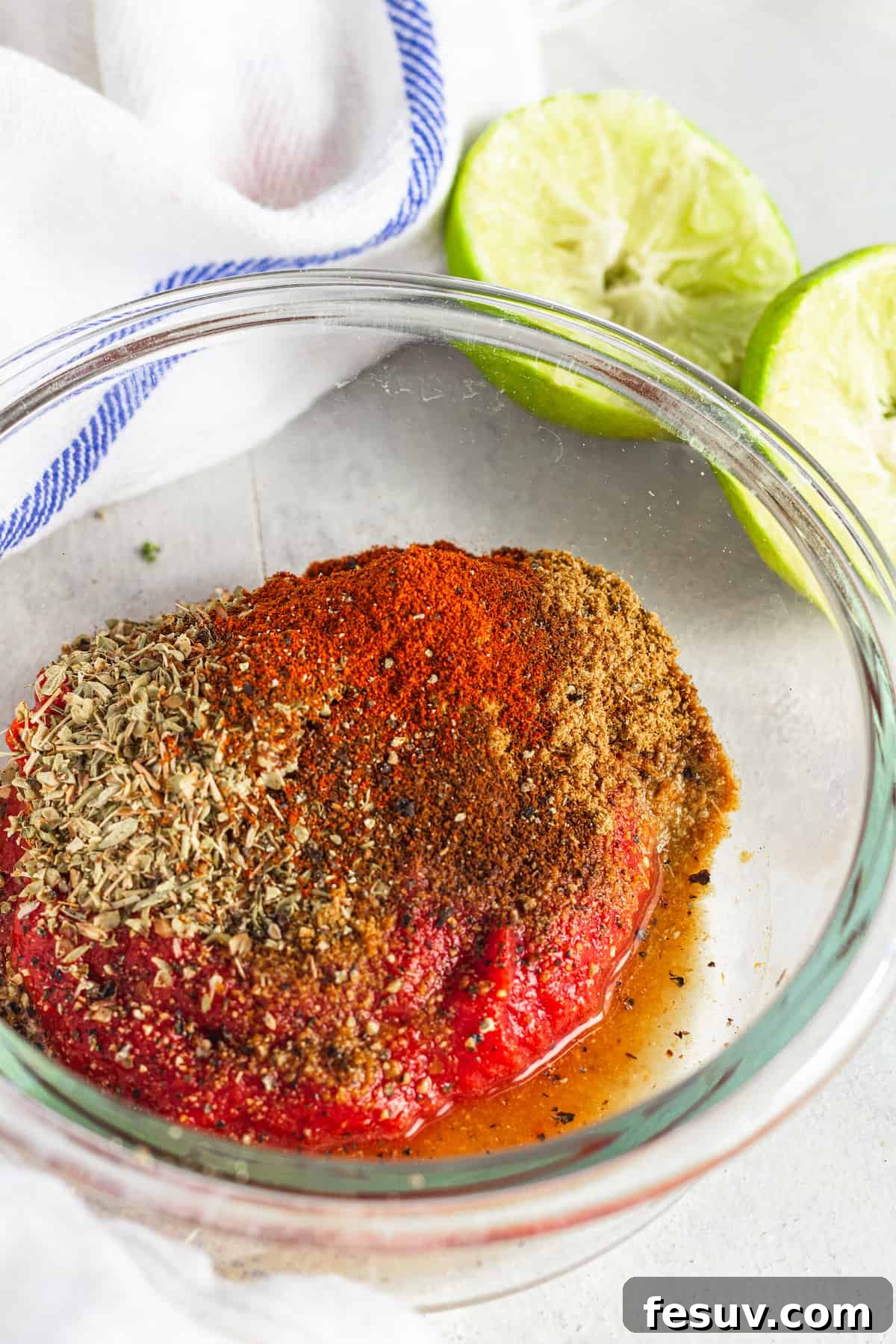 The Tomato Paste, Seasoning and Lime Juice Mixture in a Glass Bowl Beside a Juiced Lime