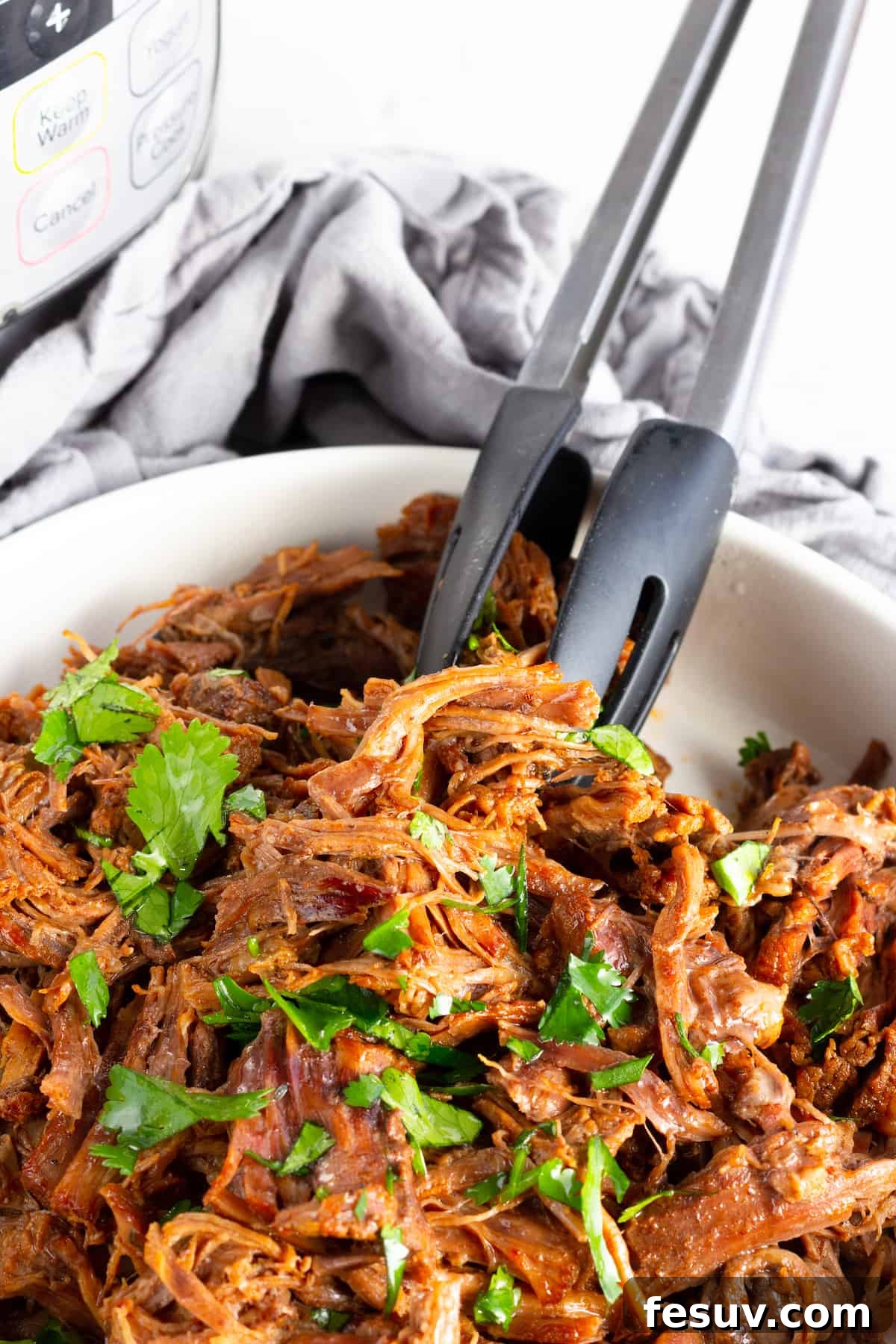 A Pair of Metal Tongs Digging Into a Bowl of Instant Pot Beef