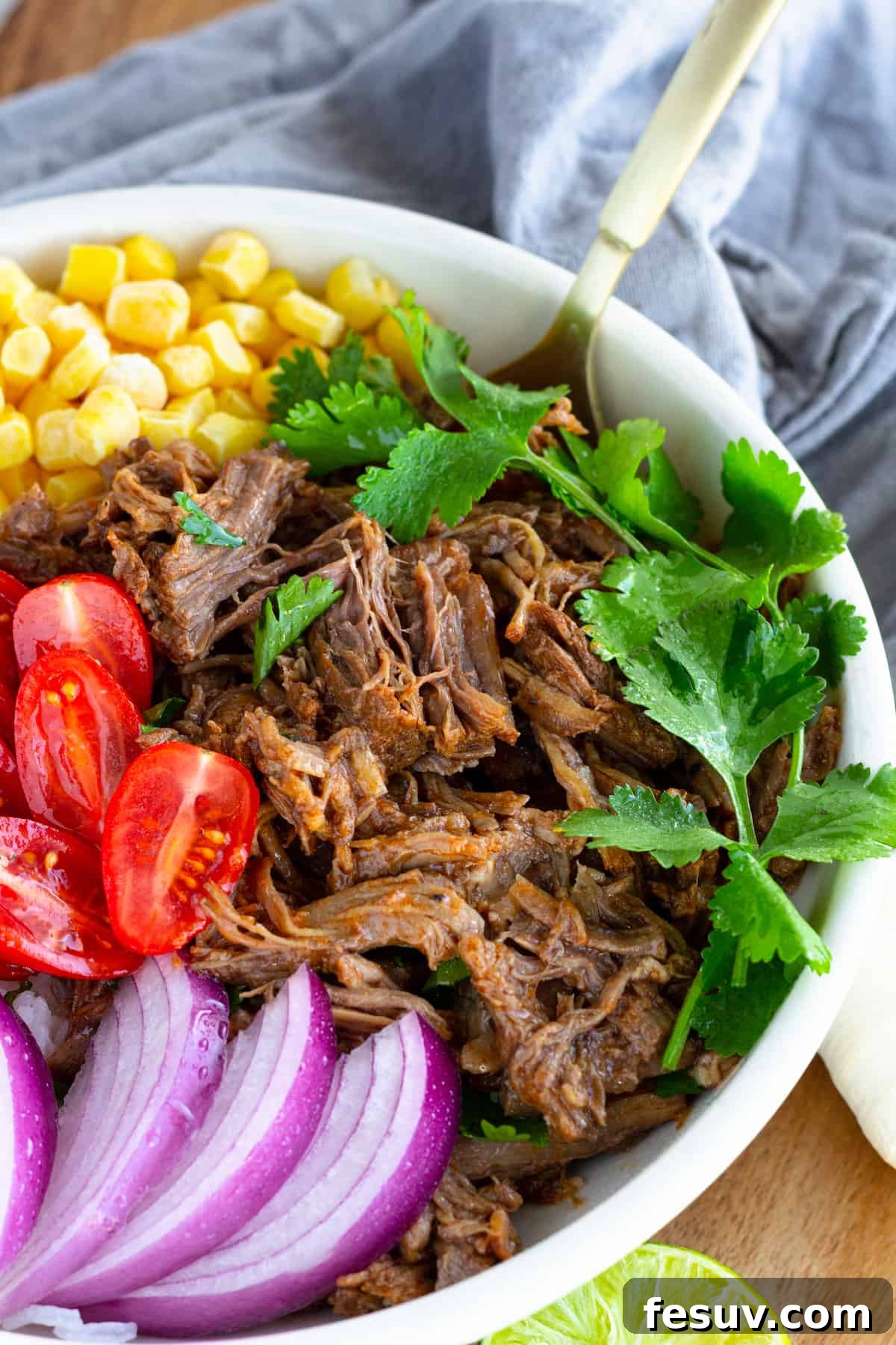 A Beef Barbacoa Burrito Bowl with a Parsley Garnish and a Golden Spoon Inside