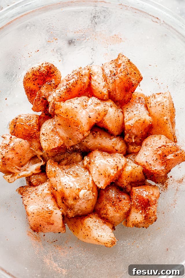 Chicken cubes seasoned with taco spice blend. Raw cubes of chicken breast seasoned with vibrant taco seasoning, ready for cooking.