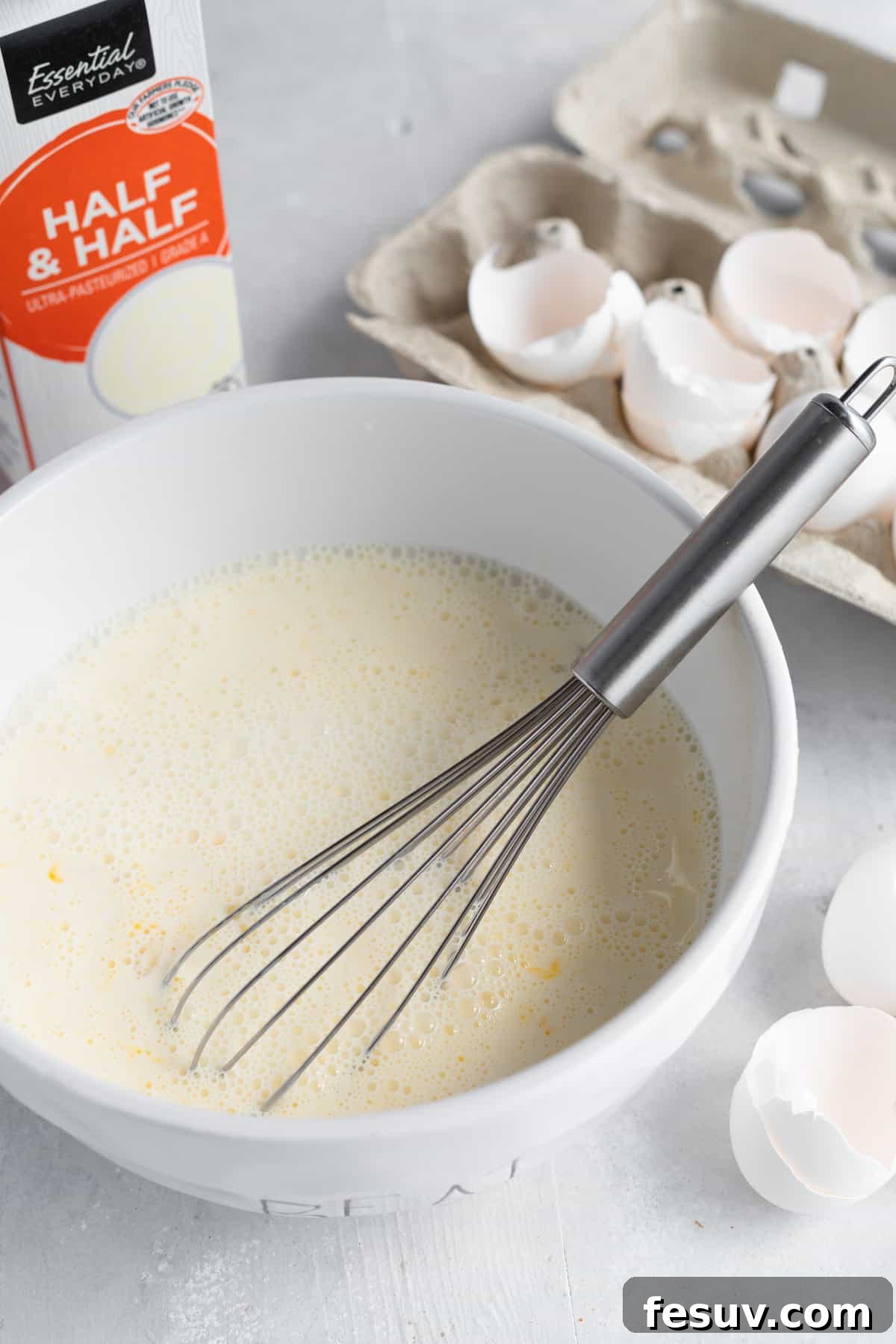 Sweet Blueberry French Toast Bake 6 A Smooth Egg Mixture in a White Bowl with a Metal Whisk, with Empty Egg Shells in the Background