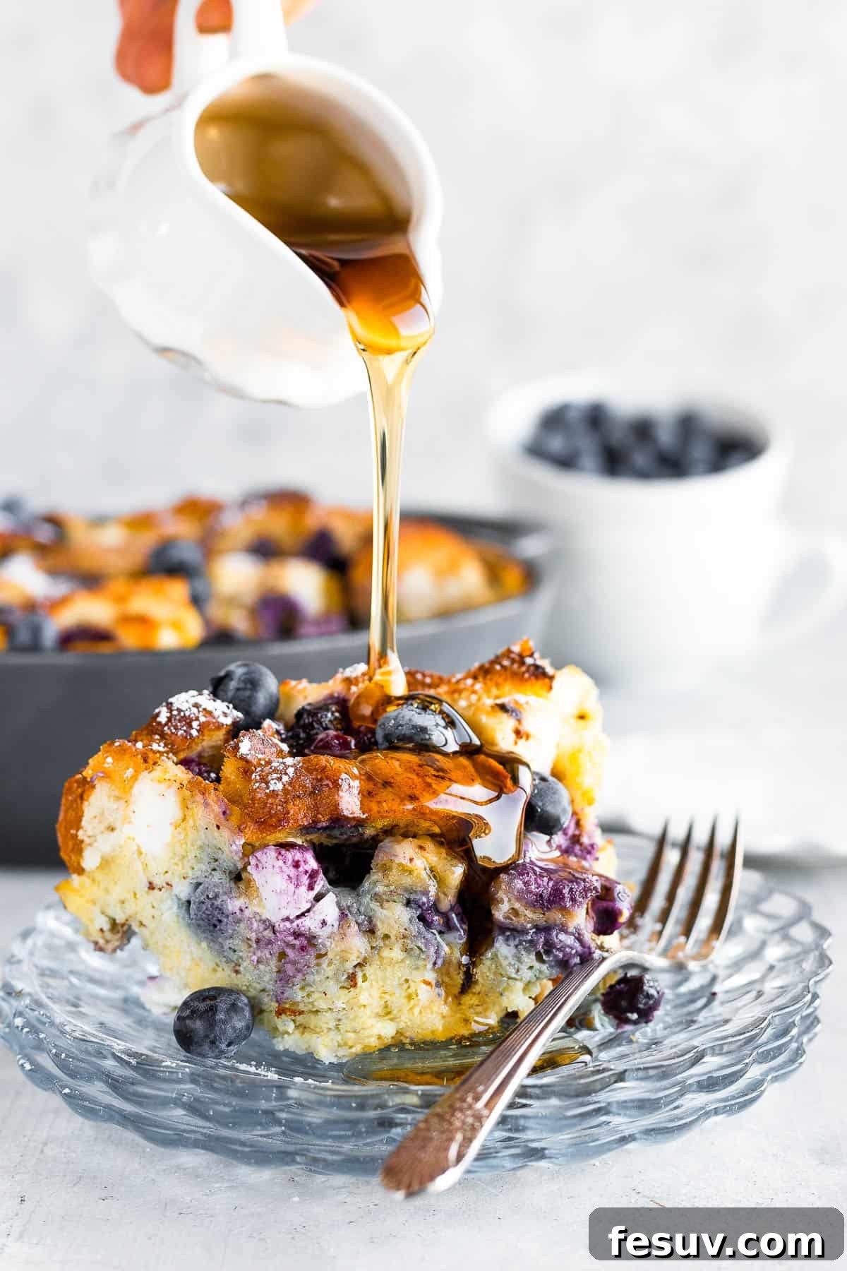 Sweet Blueberry French Toast Bake 8 A Spouted Measuring Cup Drizzling Golden Maple Syrup Over a Piece of Baked Blueberry French Toast Casserole on a Plate