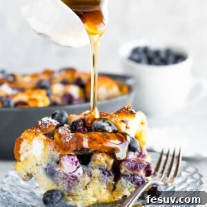 A Spouted Measuring Cup Drizzling Maple Syrup Over a Piece of Baked Blueberry French Toast Casserole