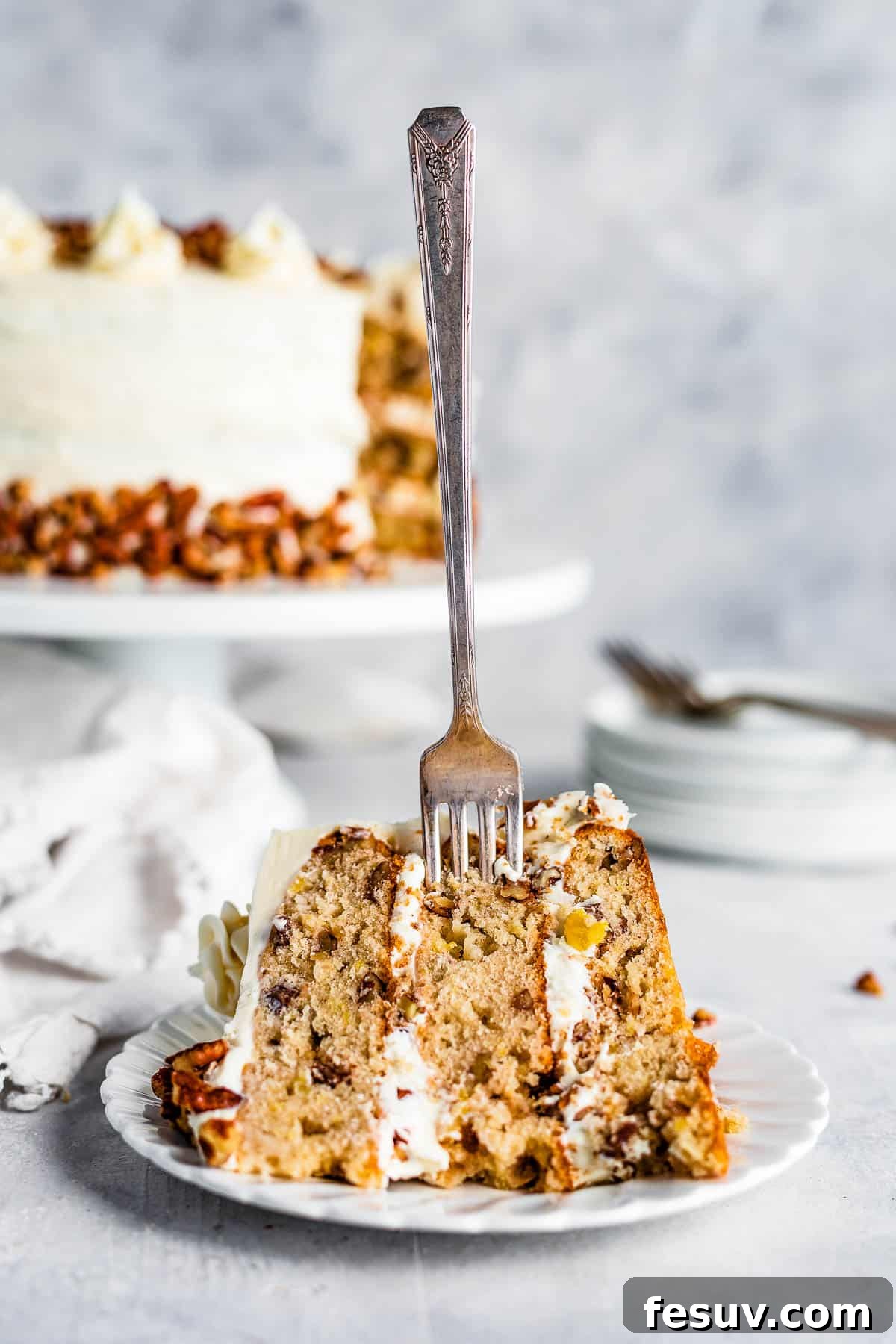 A close-up shot of a fork piercing a slice of Hummingbird Cake, revealing the moist crumb and generous frosting.