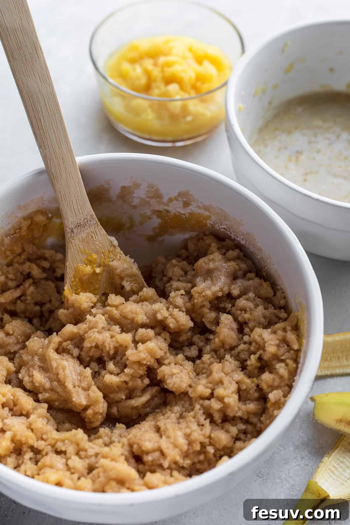 Smooth Hummingbird Cake batter in a white mixing bowl, with a banana peel nearby, indicating freshness.