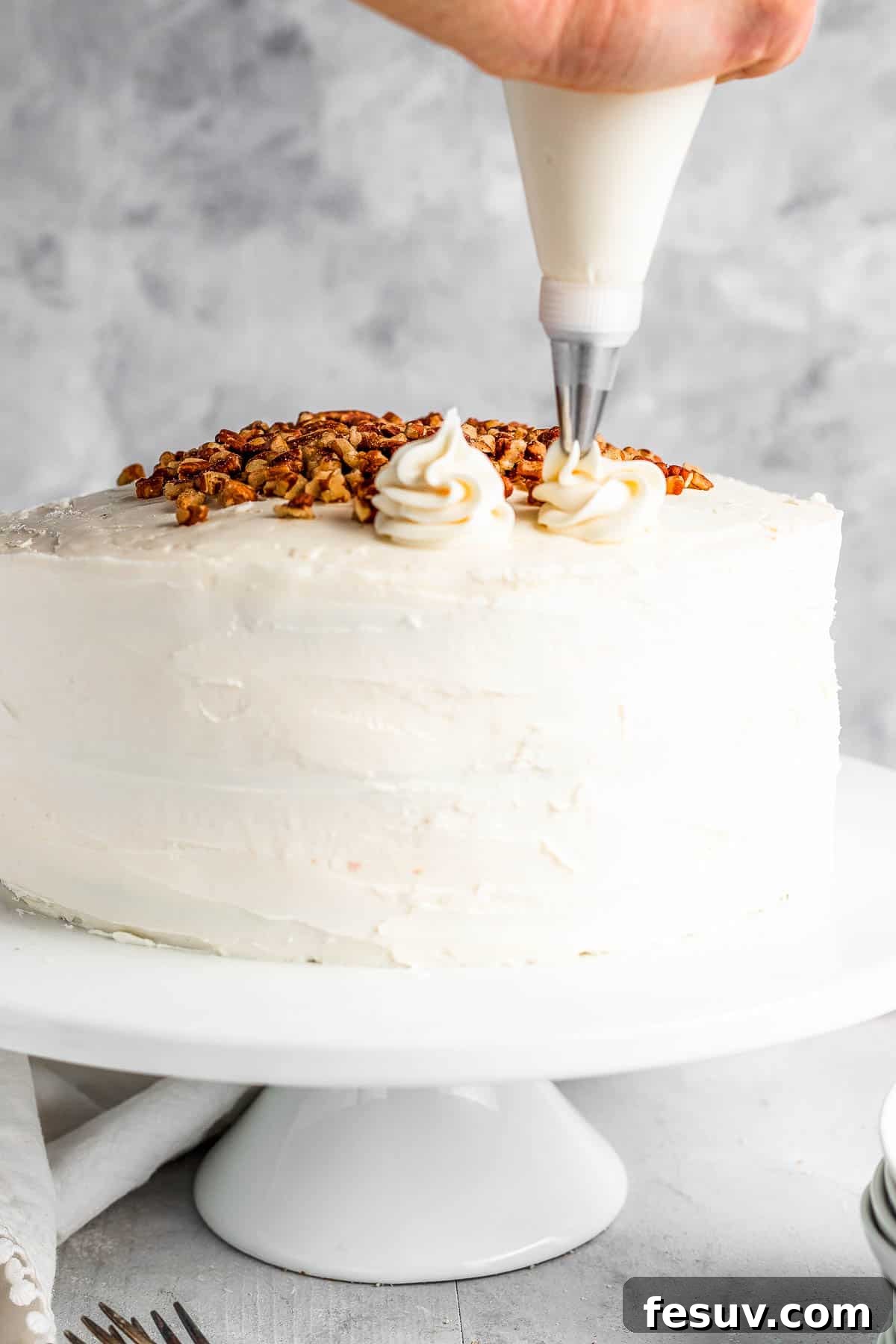 A piping tip creating beautiful swirls of cream cheese icing onto the top of a frosted Hummingbird Cake.
