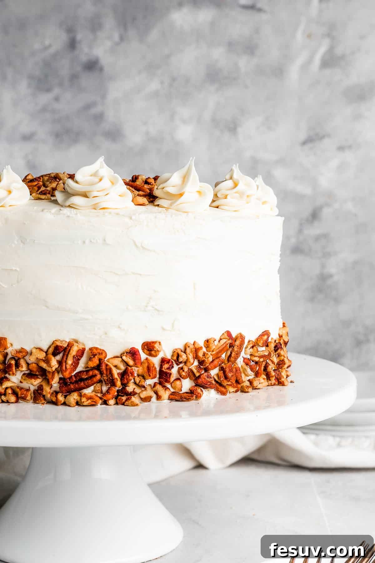 A stunning, fully frosted Hummingbird Cake, garnished with pecans, sitting proudly on a white cake stand.