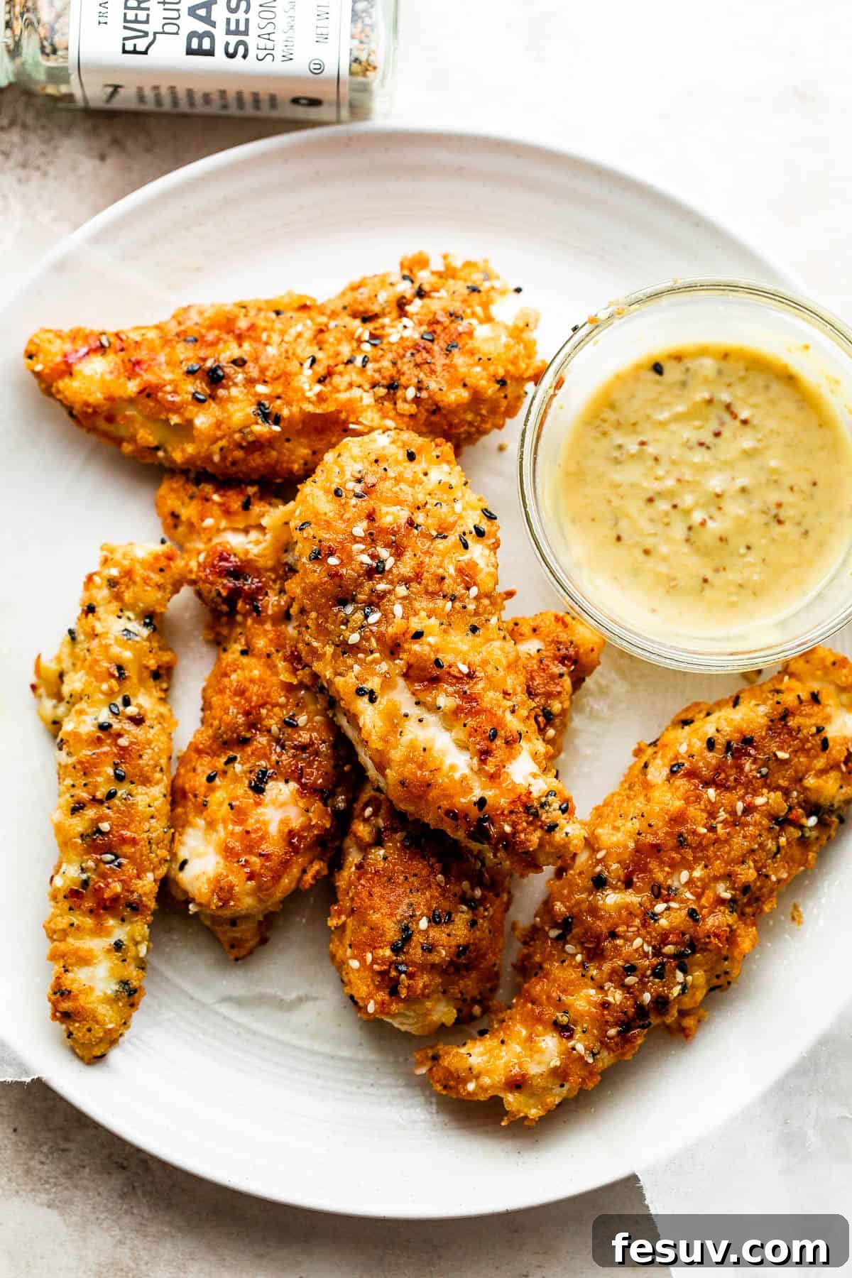 Everything Bagel Chicken Tenders arranged on a round plate and served with honey mustard dipping sauce