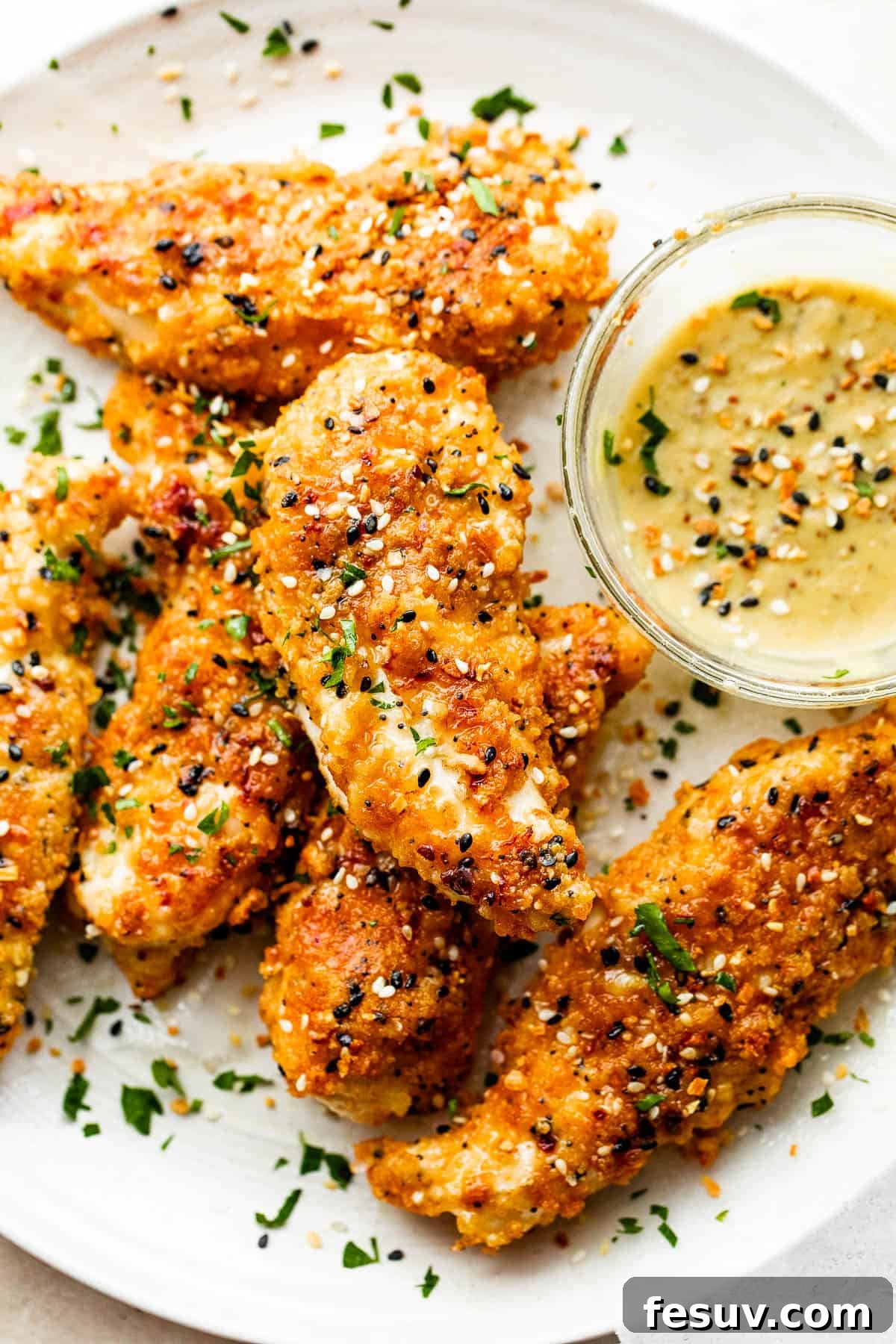 close up of six Everything Bagel Chicken Tenders arranged on a round plate and served with honey mustard dipping sauce