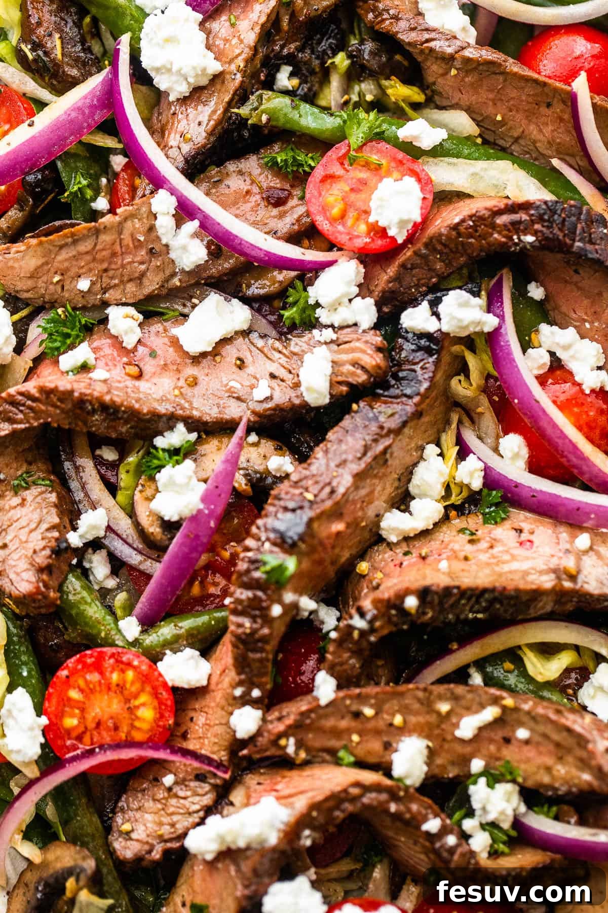 up close photo of Steak Salad on a long plate topped with cheese crumbles, tomatoes, and mushrooms