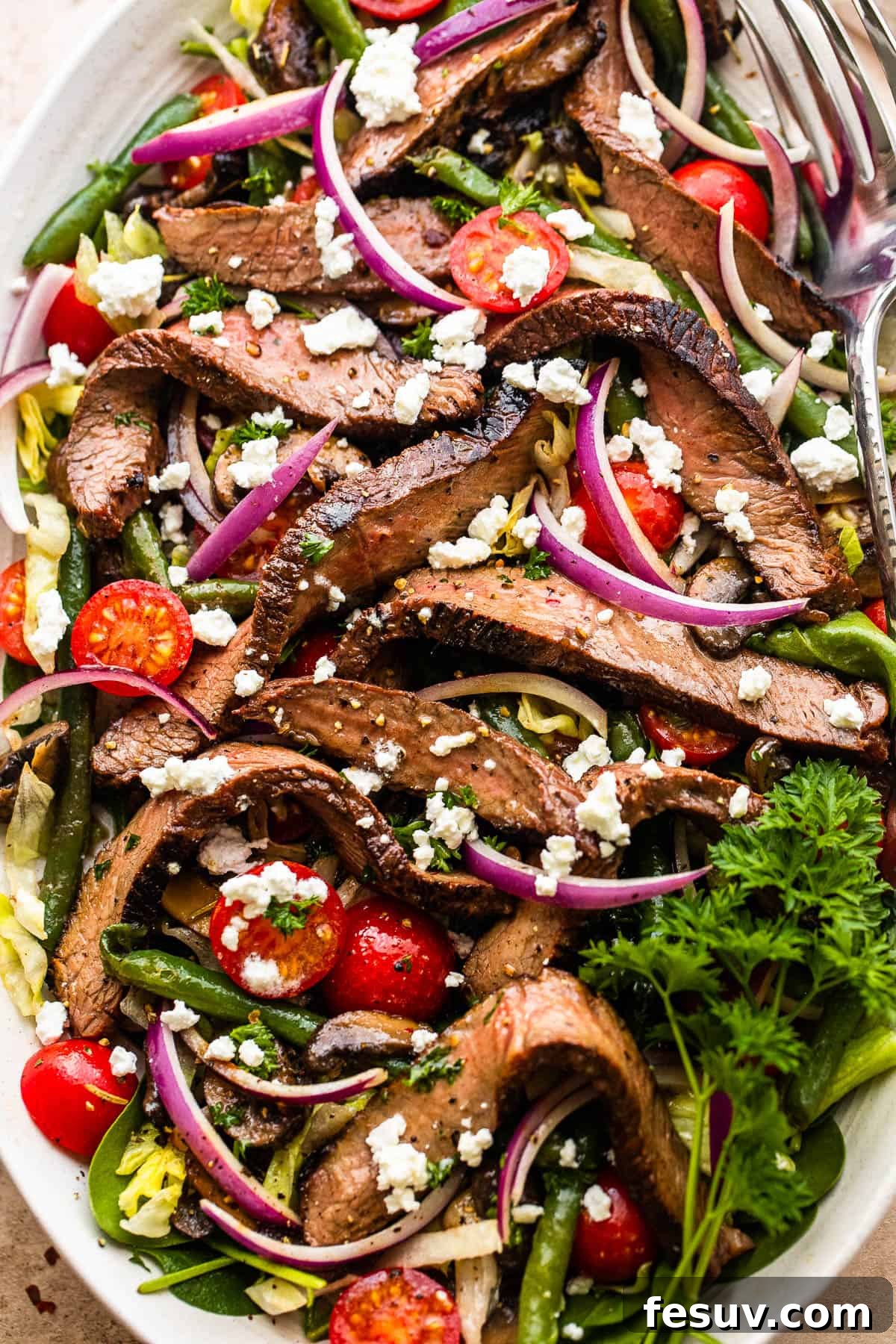 Steak Salad on a long plate topped with cheese crumbles, tomatoes, and mushrooms