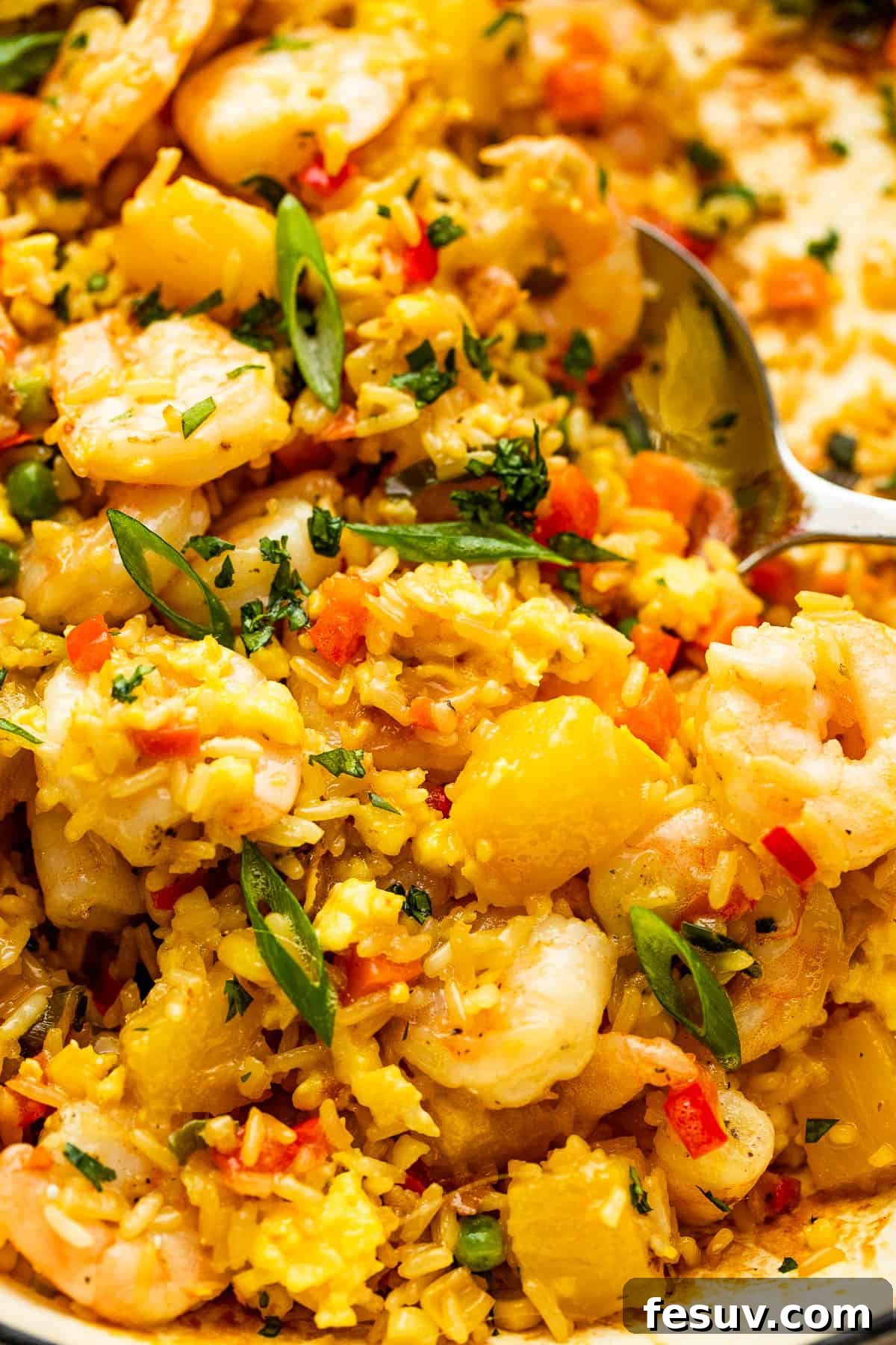 Tropical Pineapple Shrimp Fried Rice 3 A large stainless spoon scooping a portion of Shrimp Fried Rice with visible shrimp, pineapple, and vegetables from a white cast iron skillet.