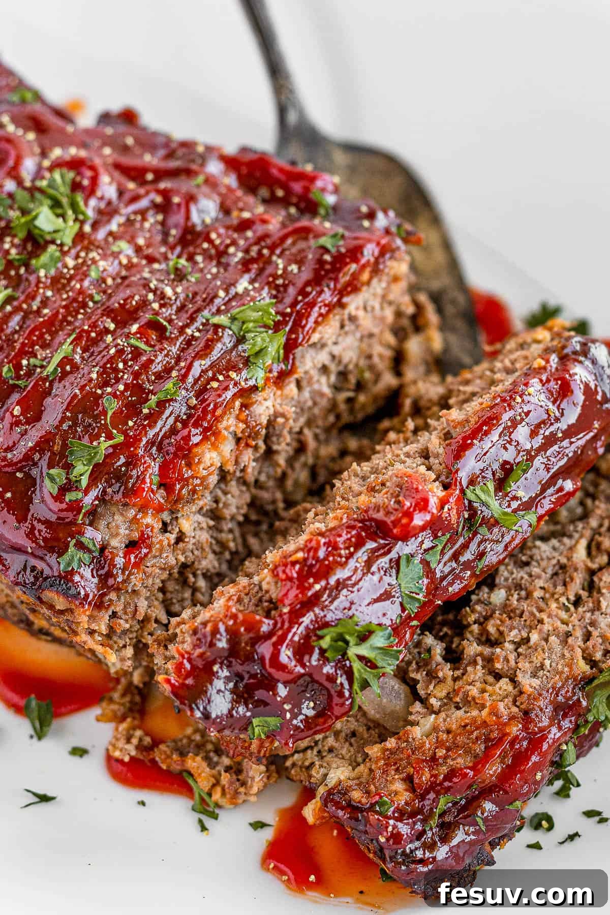 A family-friendly classic, this easy meatloaf recipe gets extra flavor from barbecue sauce, plenty of garlic, and Italian seasoning. Meatloaf Covered in Barbecue Sauce on a White Serving Platter, garnished with fresh parsley.