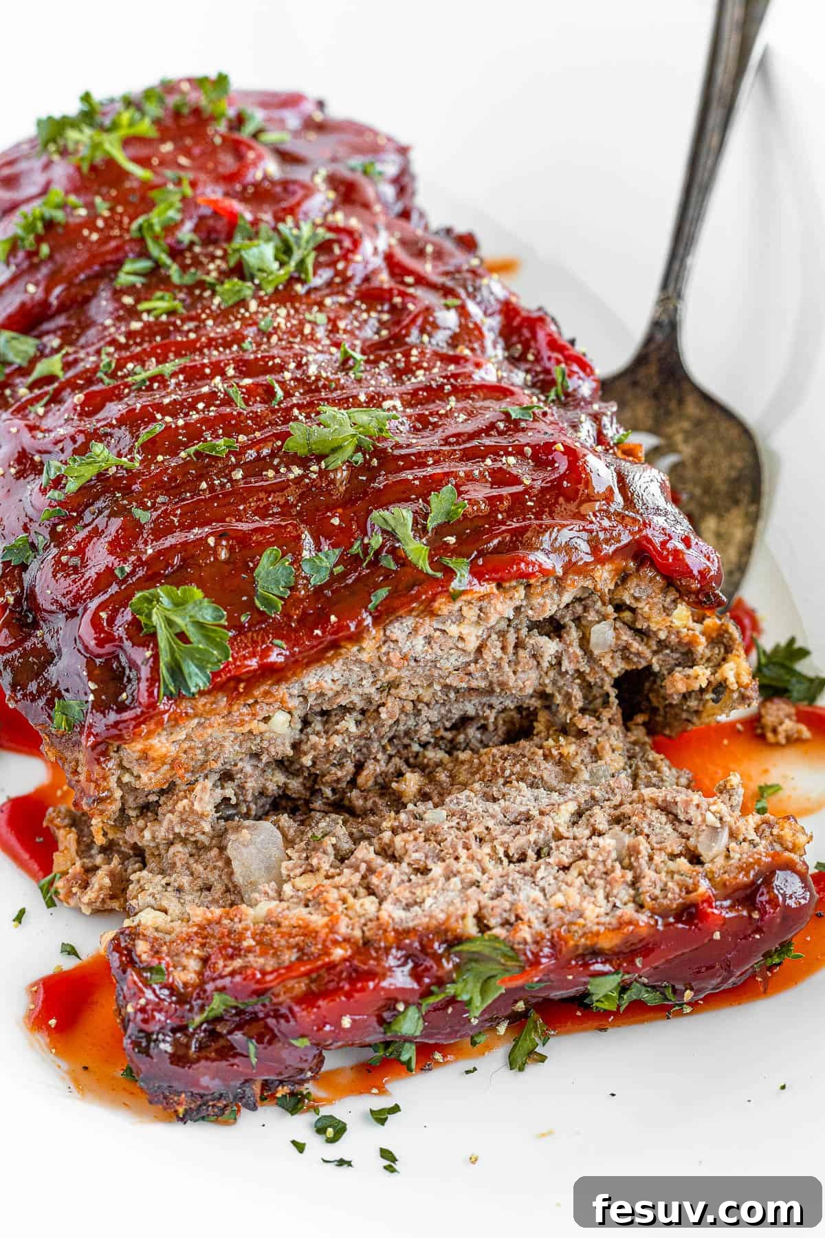 A family-friendly classic, this easy meatloaf recipe gets extra flavor from barbecue sauce, plenty of garlic, and Italian seasoning. A perfectly baked, glazed meatloaf on a white platter with one slice removed, revealing its tender interior.