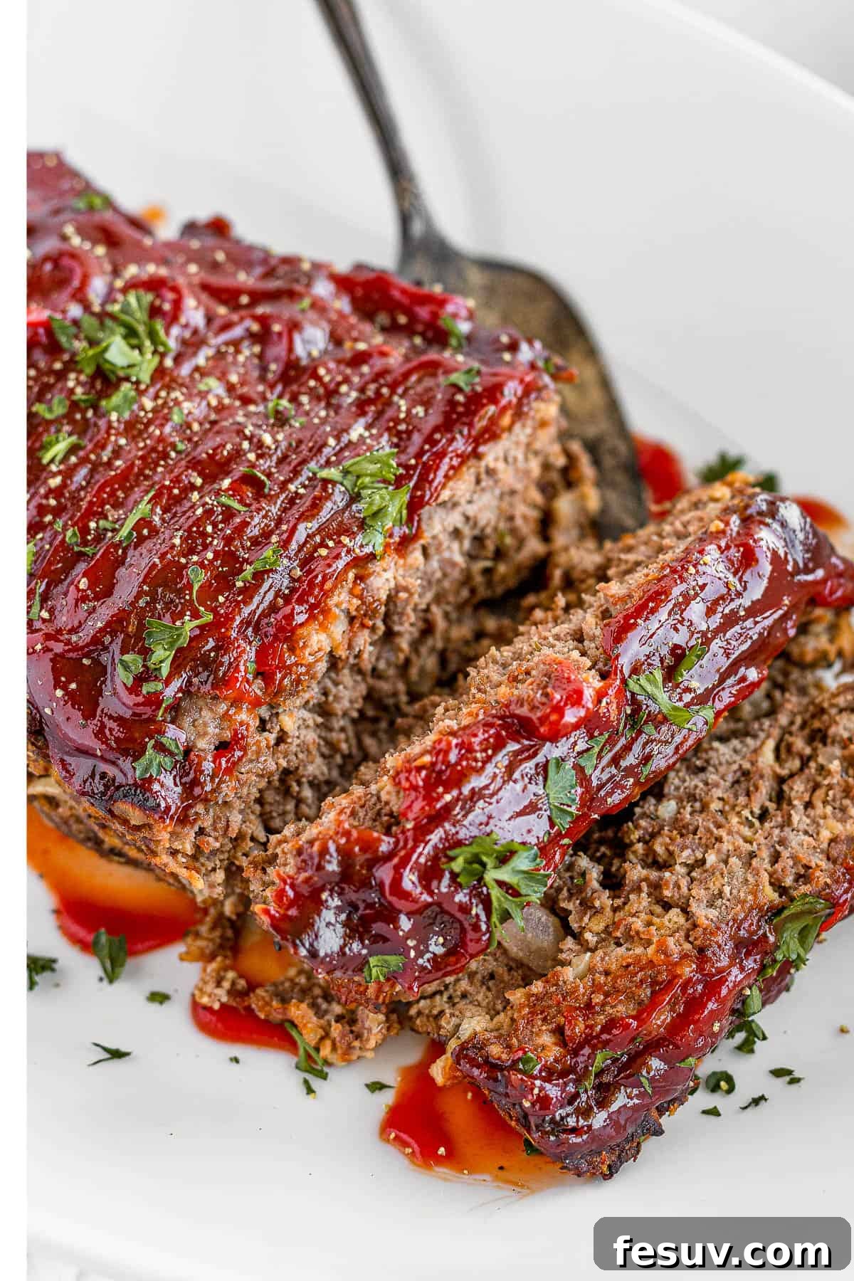 A family-friendly classic, this easy meatloaf recipe gets extra flavor from barbecue sauce, plenty of garlic, and Italian seasoning. A whole meatloaf covered in shiny barbecue sauce, placed on a white serving platter, ready to be sliced and served.