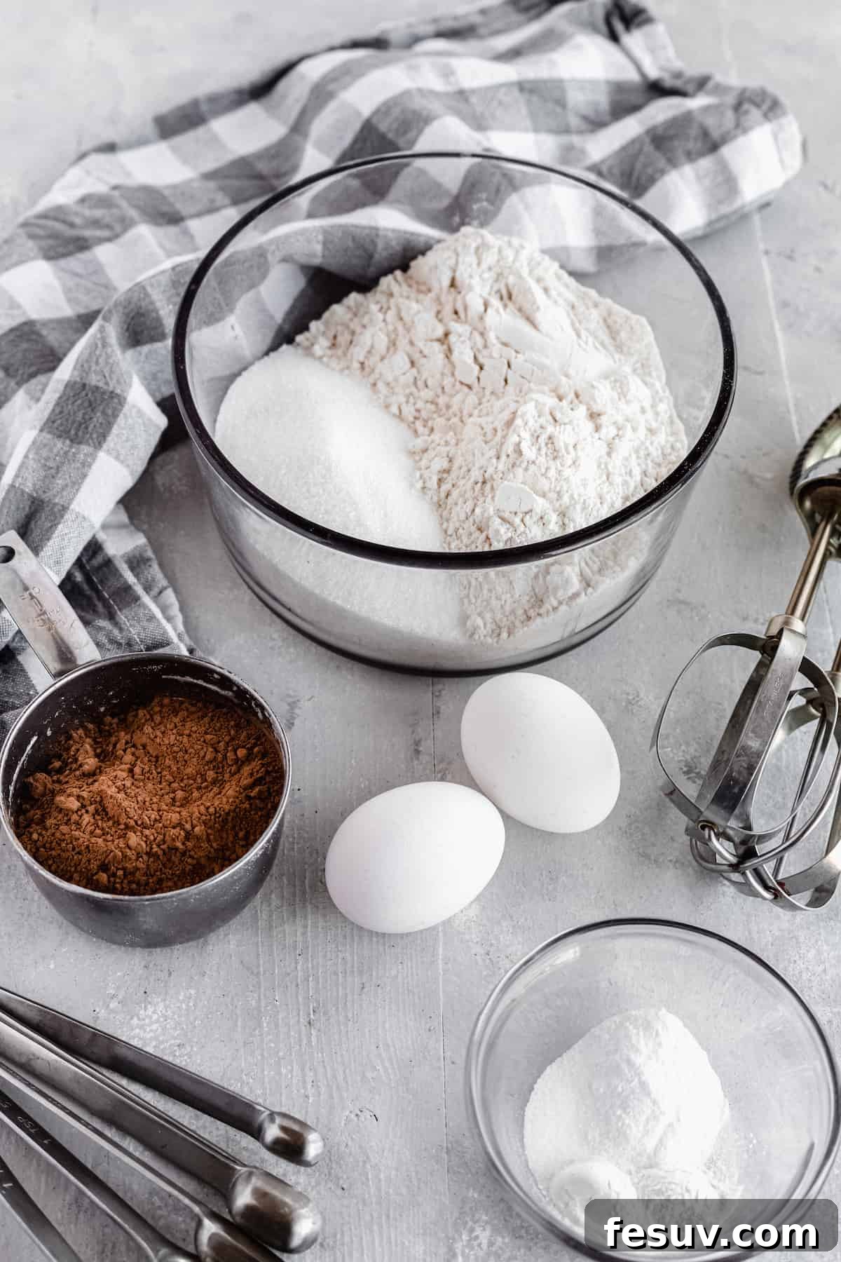 Arrangement of chocolate cake ingredients including cocoa powder, eggs, and leavening agents