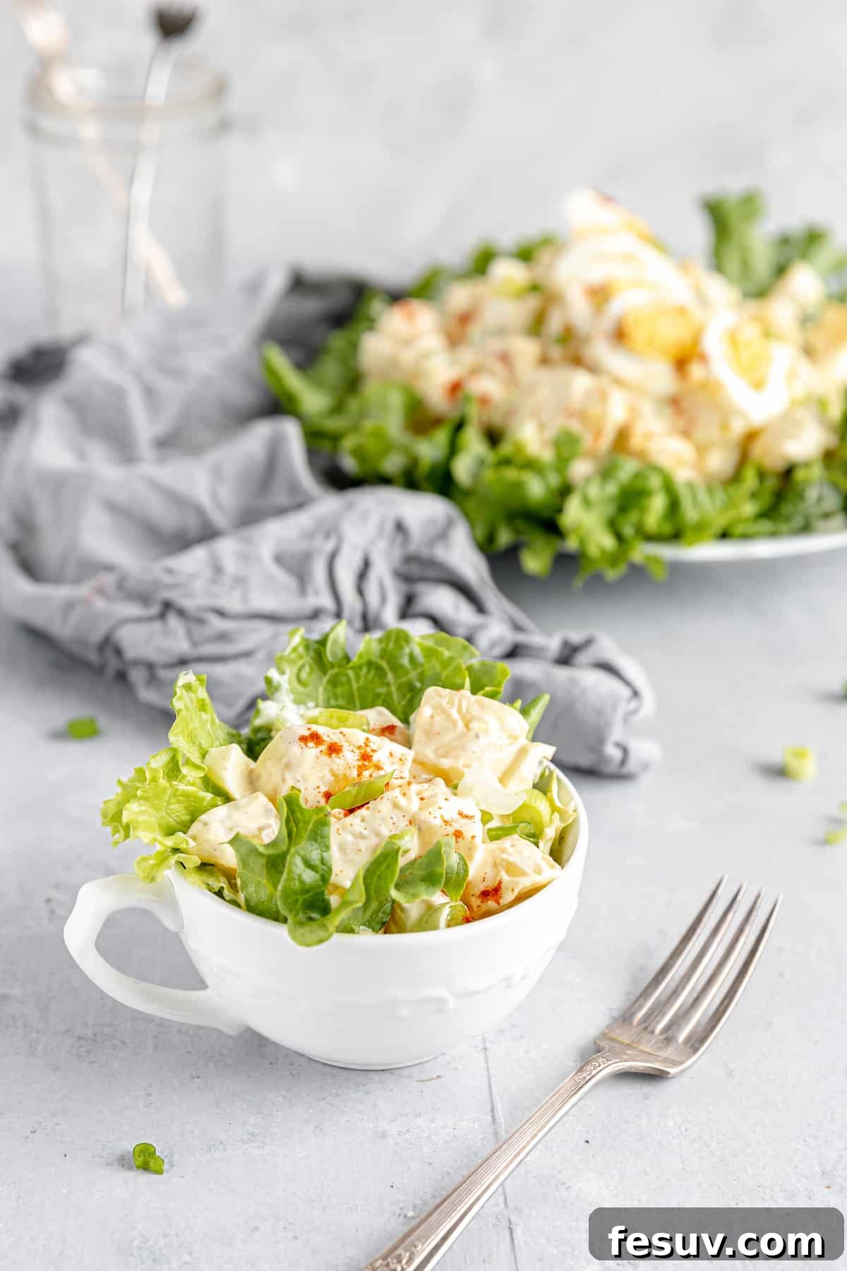 America's Favorite Potato Salad 3 A Close-Up of a Single Serving of Creamy American Potato Salad in a Mug, with a Larger Bowl in the Background, Evoking a Sense of Comfort and Home Cooking.