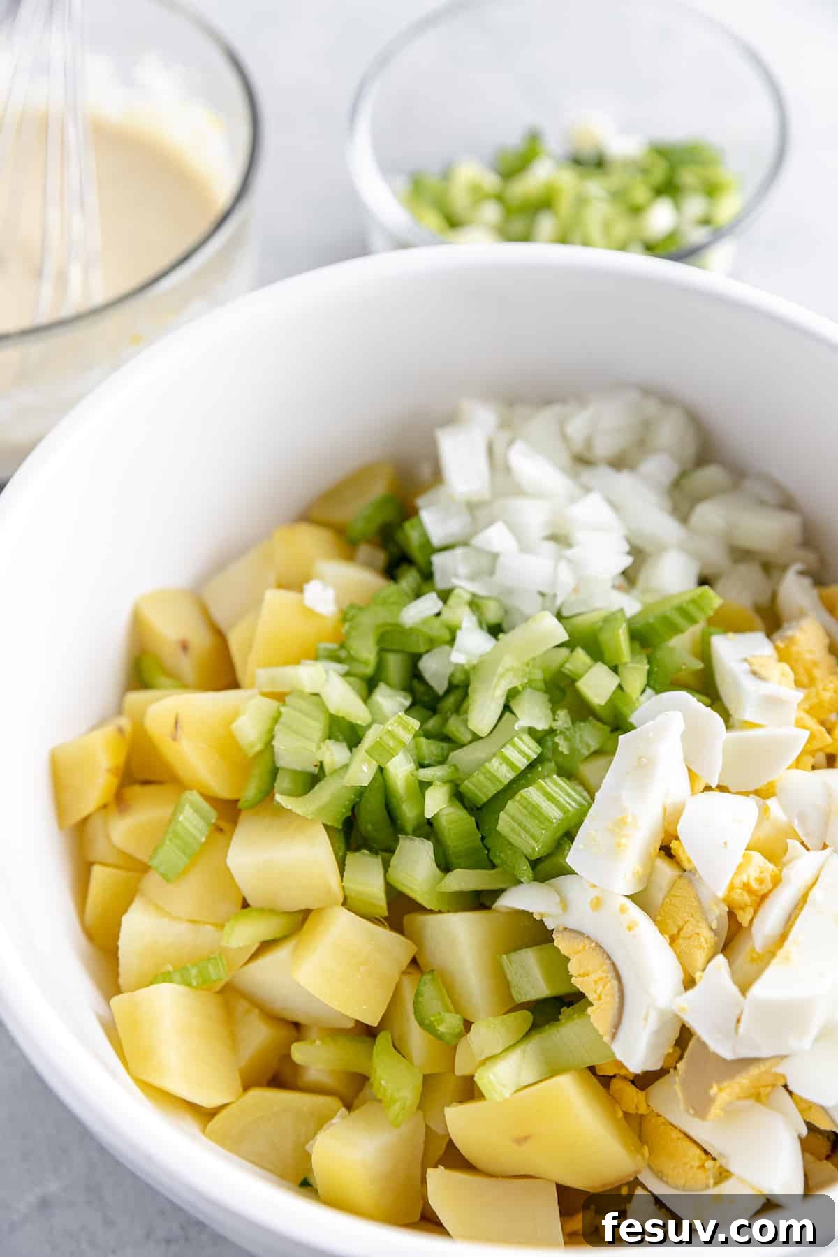America's Favorite Potato Salad 5 A White Mixing Bowl Filled with Freshly Prepared Potato Salad Ingredients – Diced Potatoes, Celery, Onion, and Hard-Boiled Eggs – Awaiting the Creamy Dressing.