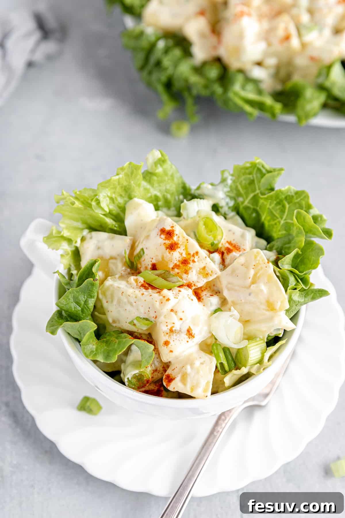 America's Favorite Potato Salad 8 A Close-Up Shot of a Hearty Serving of American Classic Potato Salad in a Tall Cup, Nestled Among Fresh Lettuce Leaves, Highlighting its Rich and Creamy Texture.