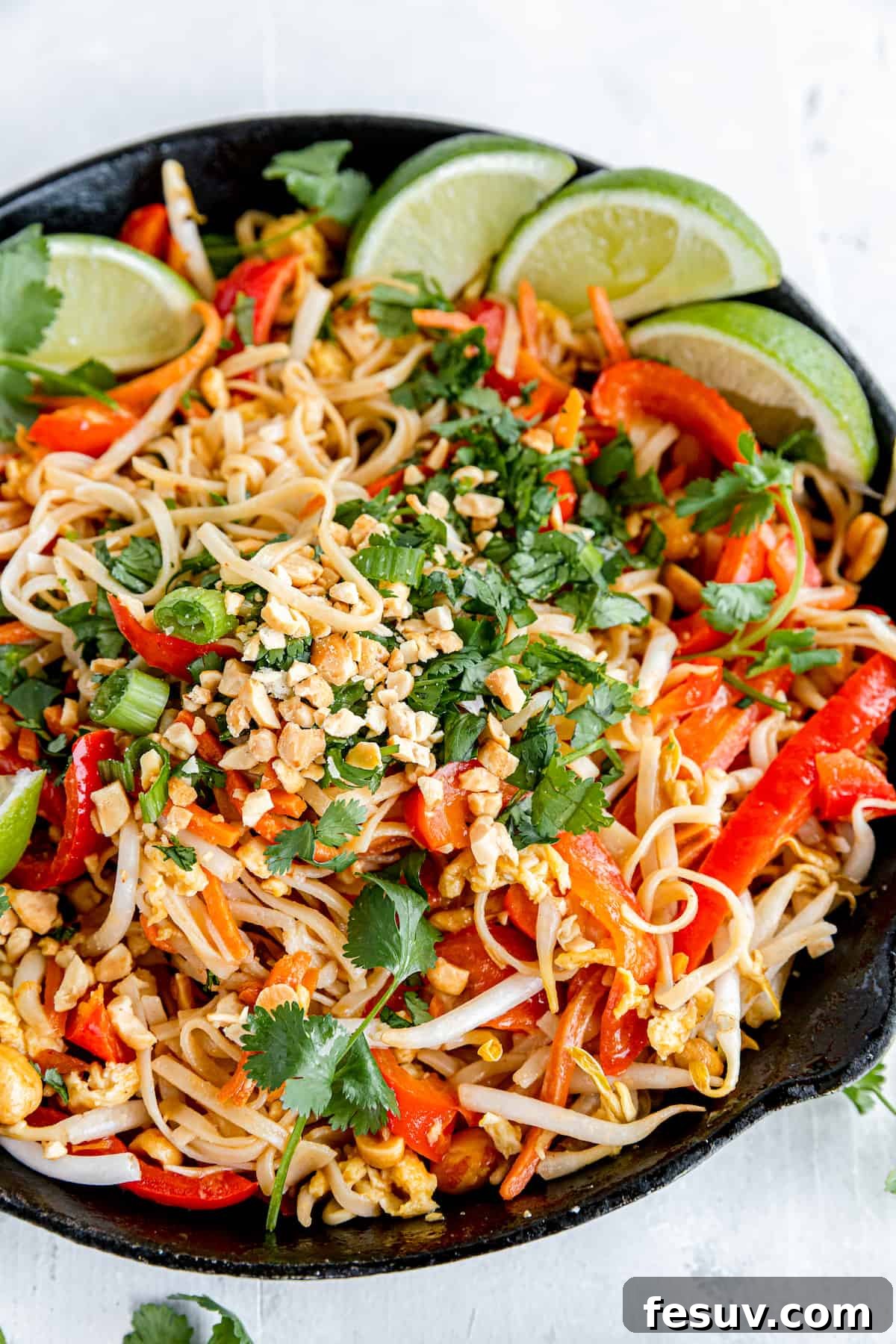 In this easy Pad Thai recipe, rice noodles are tossed with scrambled eggs, roasted peanuts, colorful veggies, and a sweet, salty, sour sauce. A Black Skillet Filled with Pad Thai on Top of a White Dinner Table