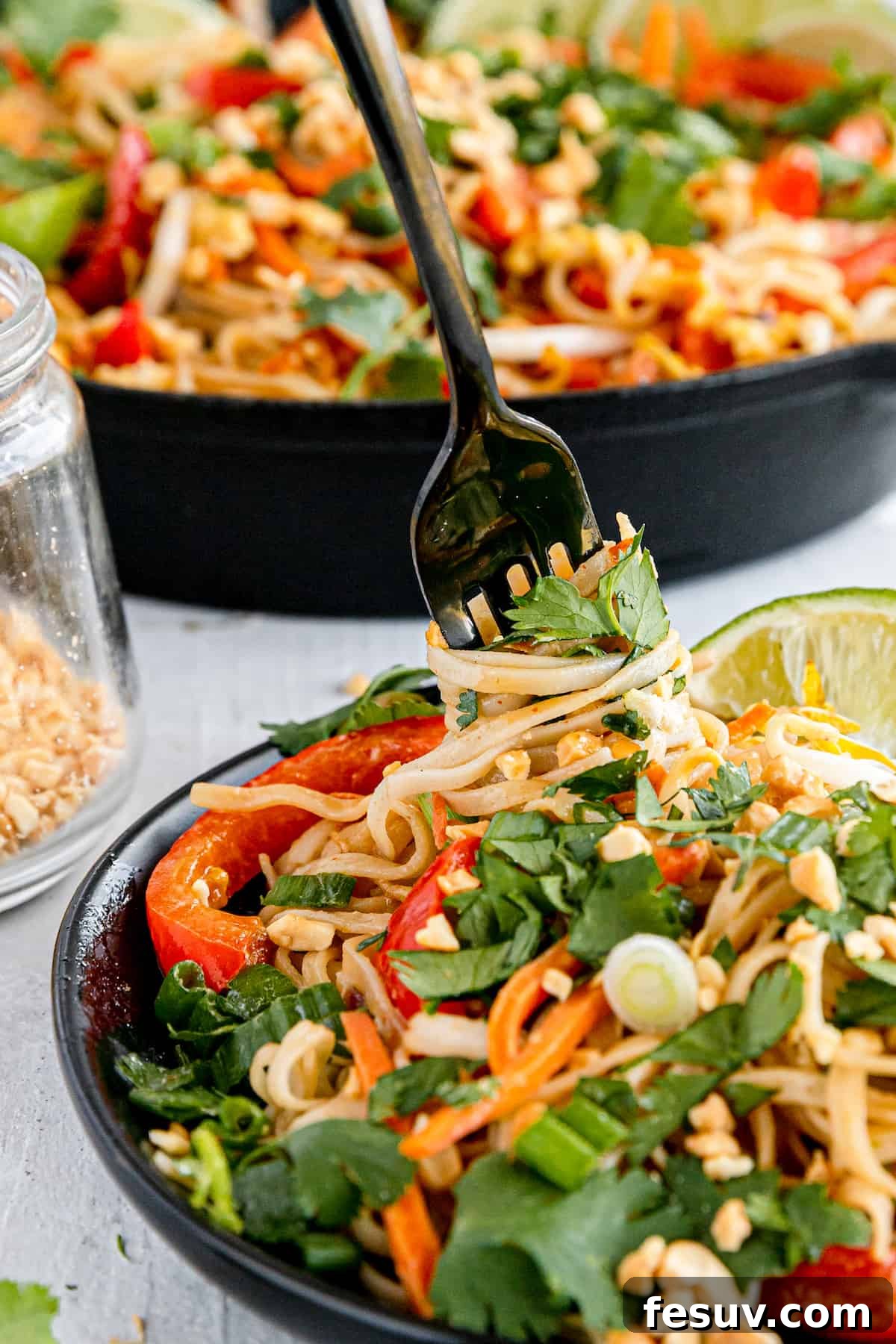 In this easy Pad Thai recipe, rice noodles are tossed with scrambled eggs, roasted peanuts, colorful veggies, and a sweet, salty, sour sauce. A Close-Up Shot of a Fork Digging Into a Plate of Pad Thai
