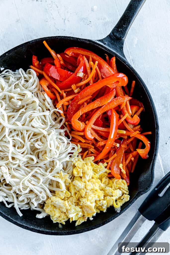 In this easy Pad Thai recipe, rice noodles are tossed with scrambled eggs, roasted peanuts, colorful veggies, and a sweet, salty, sour sauce. Scrambled Eggs, Brown Rice Noodles and Chopped Veggies Inside of a Black Skillet